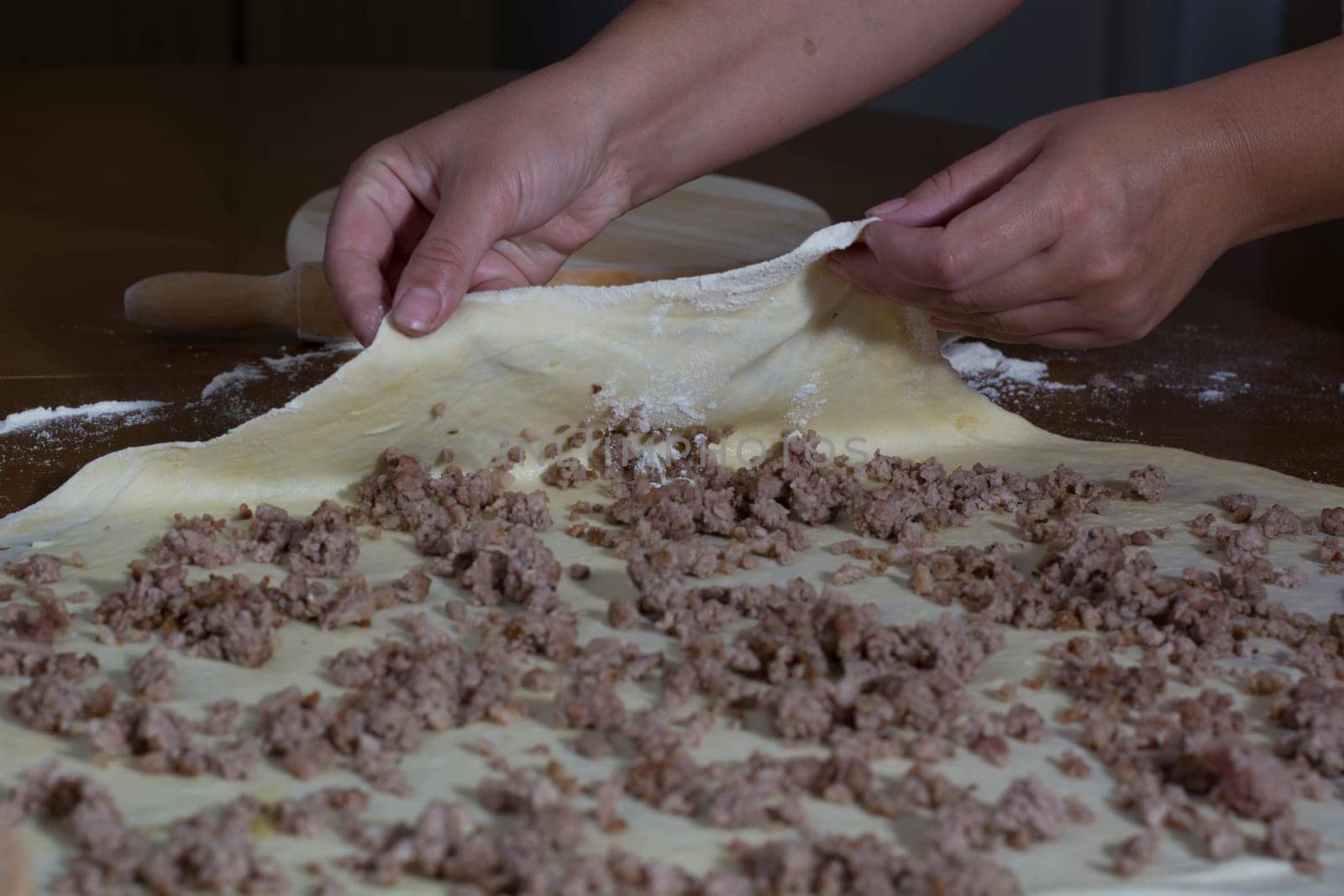 Woman making dough with meat at home on the kitchen table