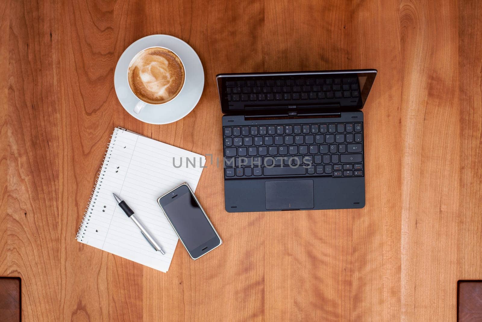 notebook,smartphone, notepad with pen and  cappuccino on wooden table from above