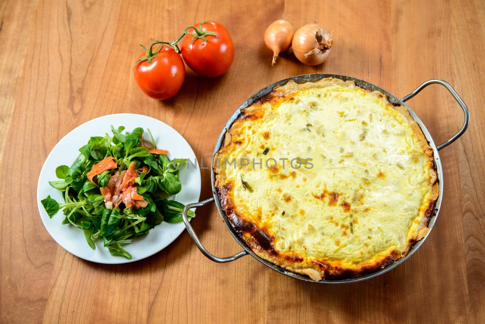 baked quiche with field salad on wooden table