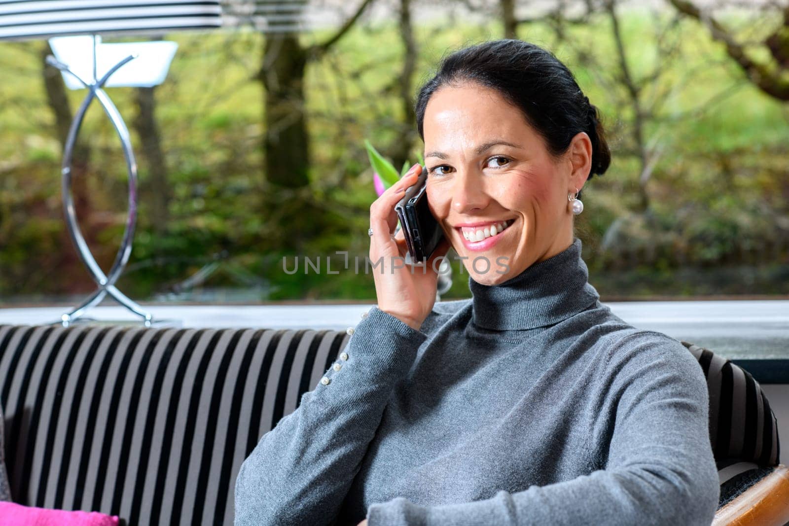 young dark haired woman at home sitting on sofa andcalling
