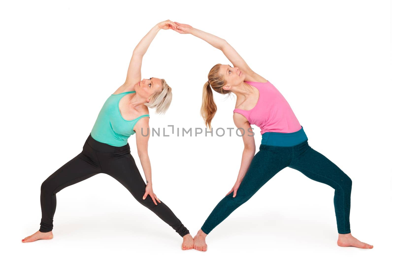 Full-body view of two young blonde women during a partner yoga exercise standing against a white background with slight shadows.