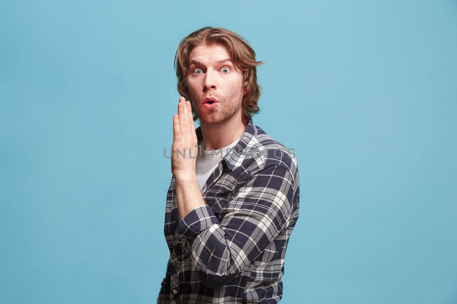Secret, gossip concept. Young man whispering a secret behind her hand. Business man isolated on trendy blue studio background. Young emotional man. Human emotions, facial expression concept.