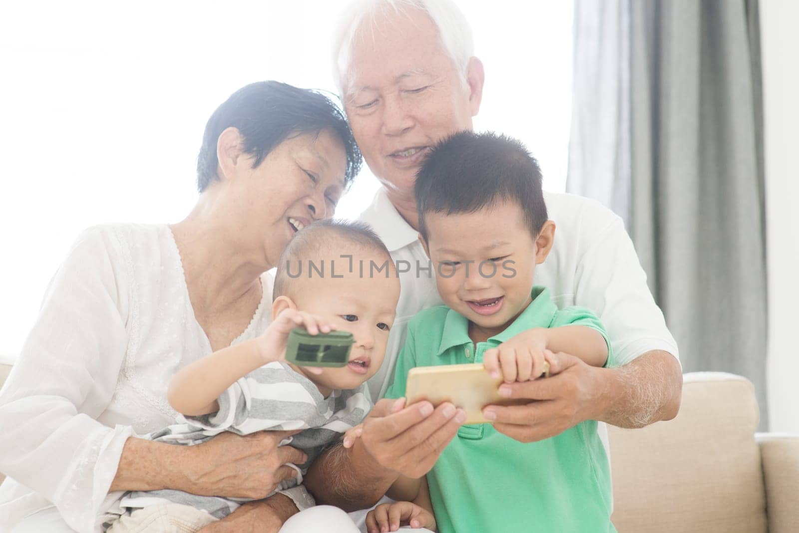 Portrait of happy Asian grandparents and grandchildren taking self photo using smart phone at home, family indoor lifestyle.