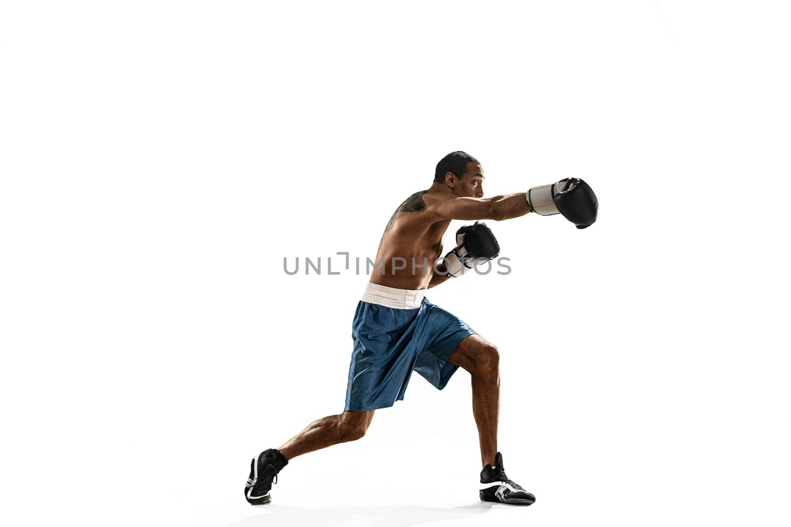 Sporty man during boxing exercises making direct hit. Photo of boxer on white background. Strength, attack and motion concept. Fit african american model in movement. Afro muscular athlete in sport uniform
