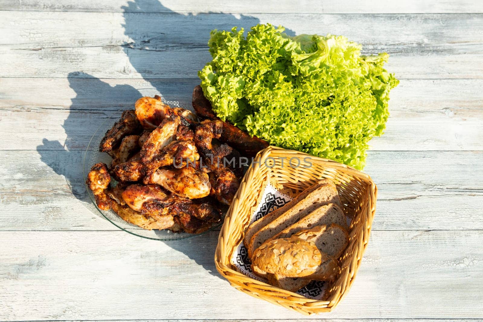 Close up on plate of fresh grilled meat surroundet by fresh salad and a whole grain bread in basked. Presented outdoor on wooden table.