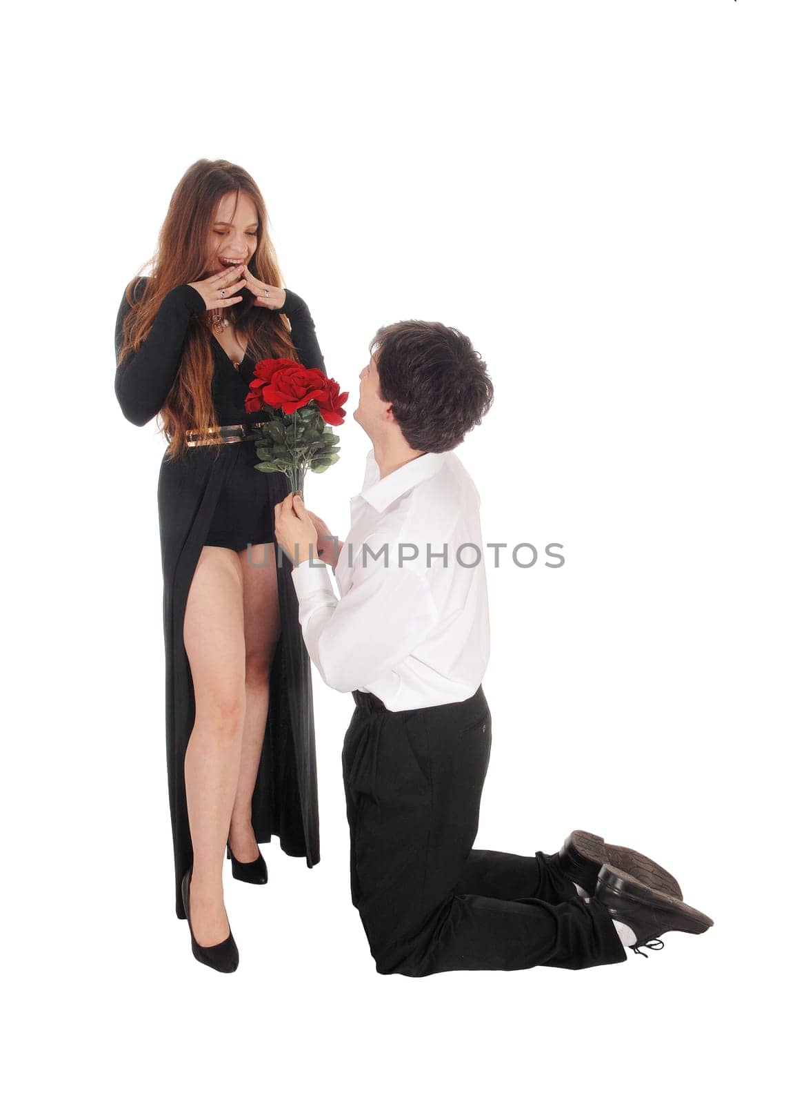 A young man kneeling in front of hid girlfriend with some red roses in.his hand, she is surprised, isolated for white background.
