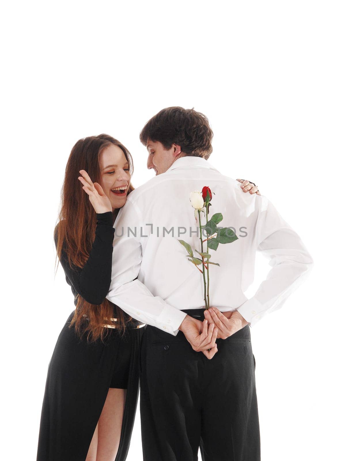 A happy young couple standing isolated for white background, he has.some roses for her to surprises his girlfriend.