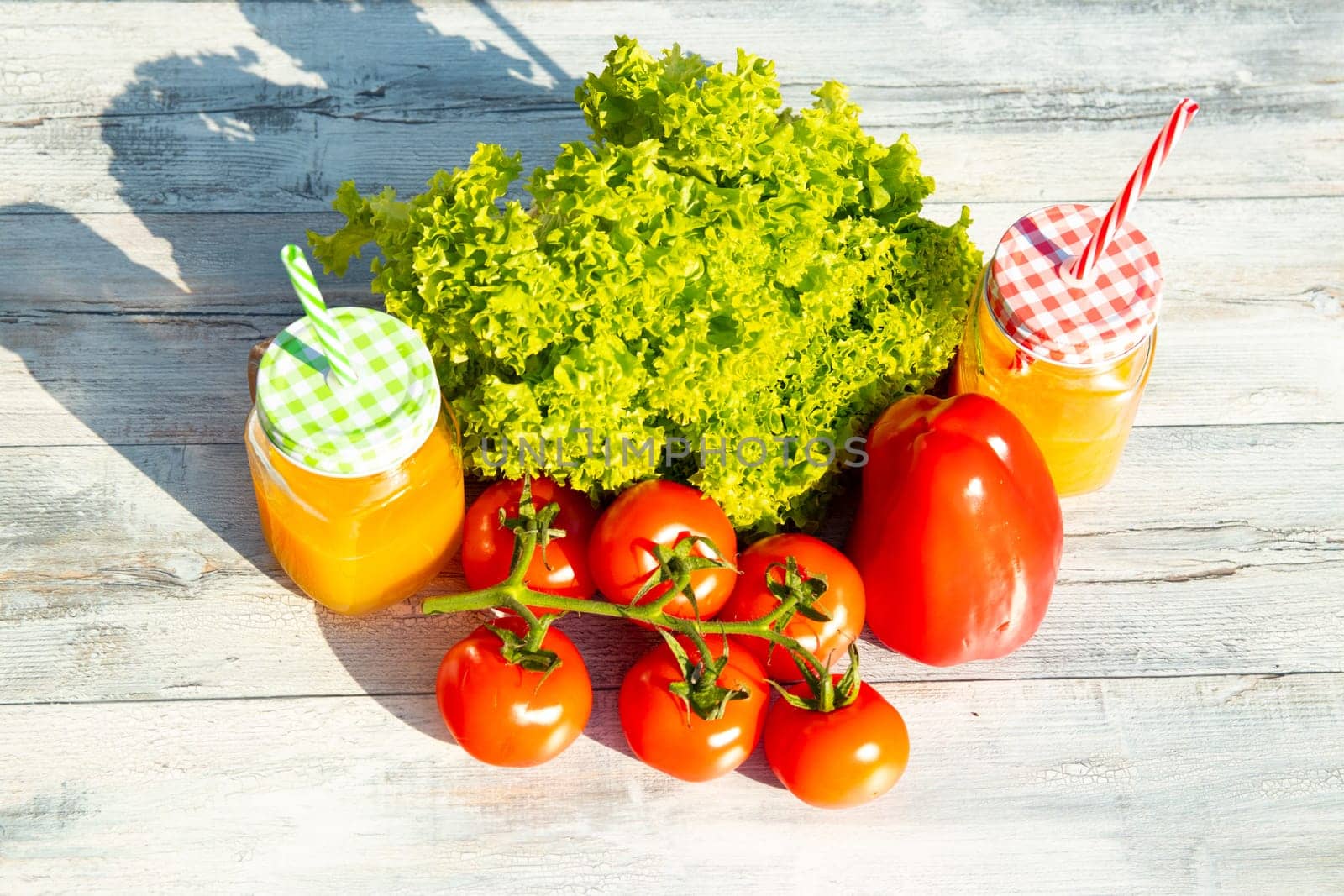 Healthy fresh salad, tomatoes, paprika and two glasses filled with fresh pressed orange juice. Presented outdoor on bright wooden table. Food health concept. .