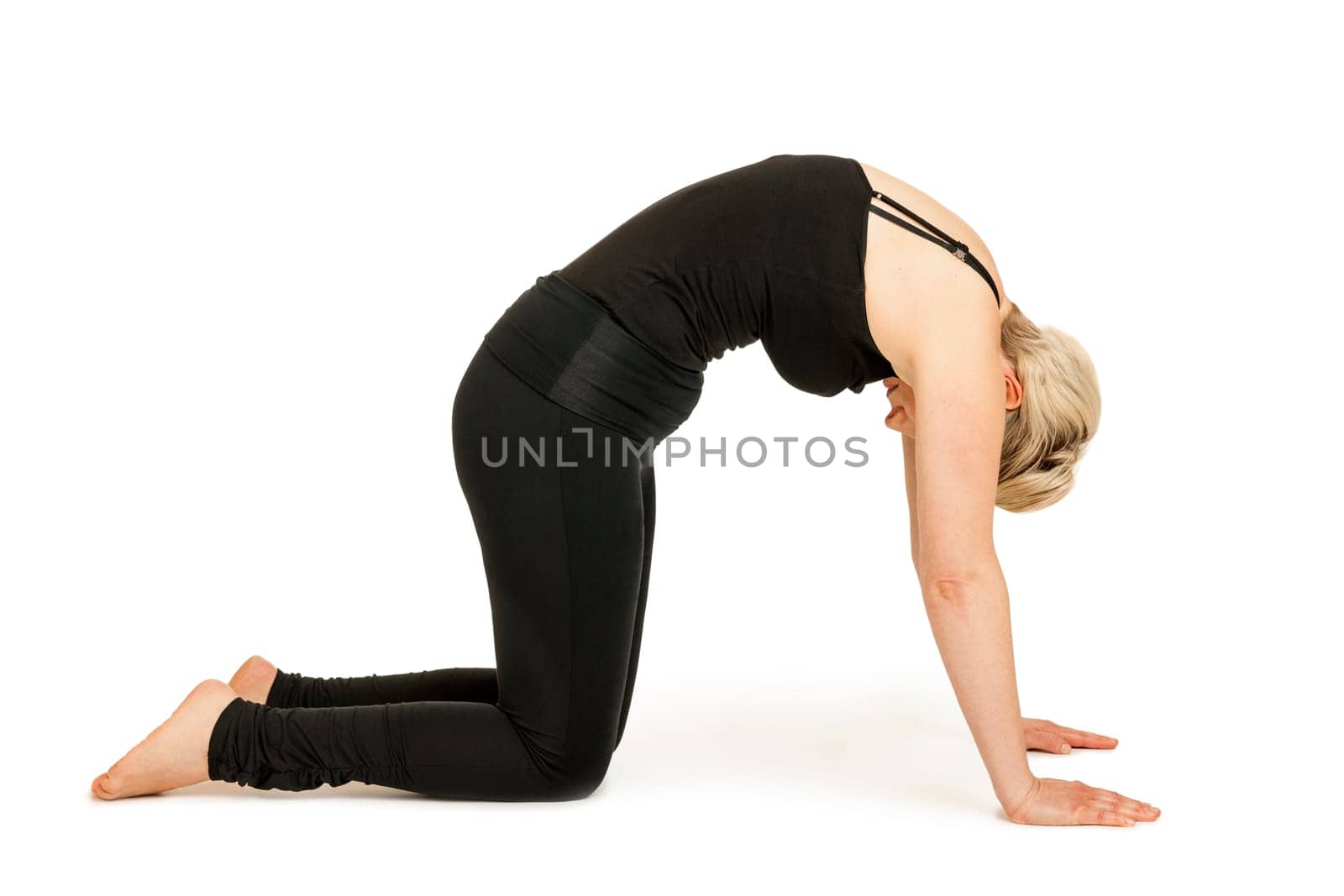 Lateral full-body view of a young woman against a white background showing the yoga exercise the cat (Marjaryasana).