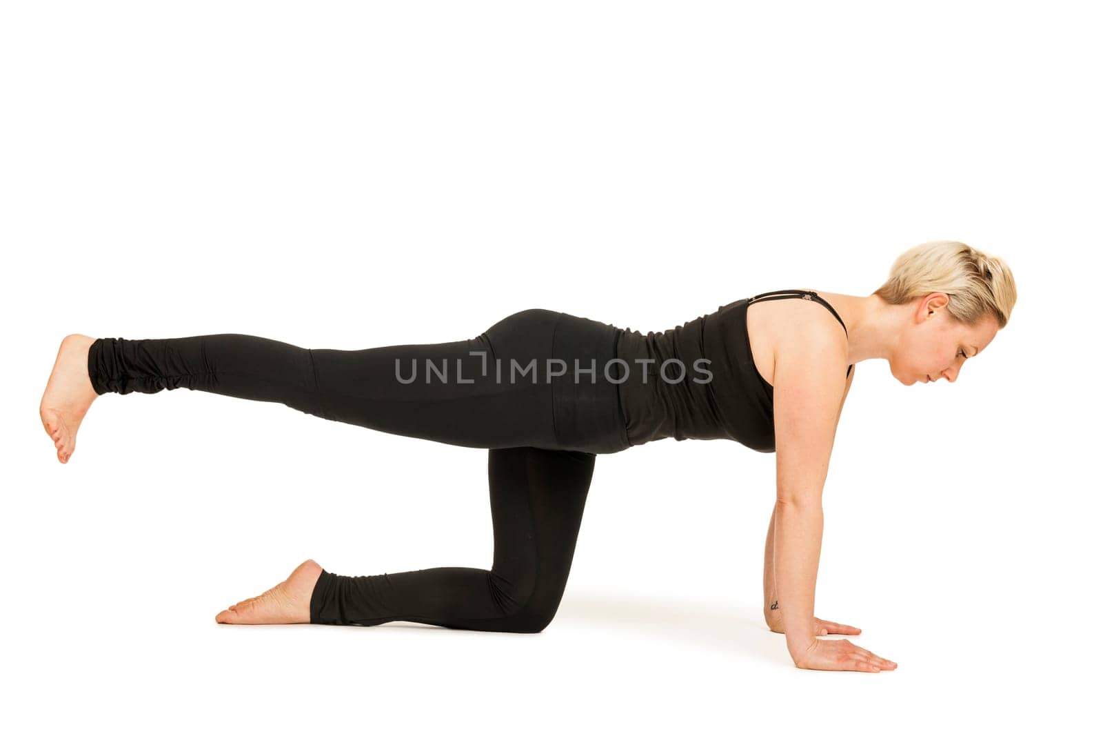 Lateral full-body view of a young woman against a white background showing the yoga exercise "cat"" (Majariasana)."
