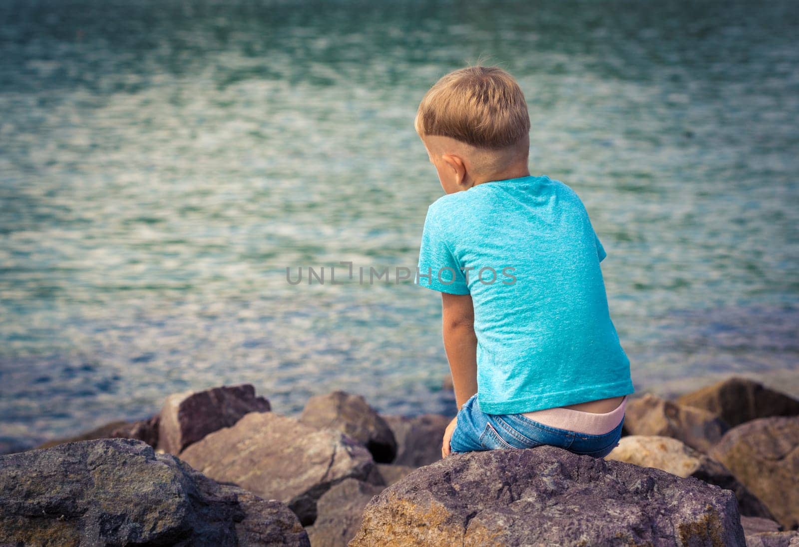Cute caucasian boy at seaside. Rear view. Leisure time