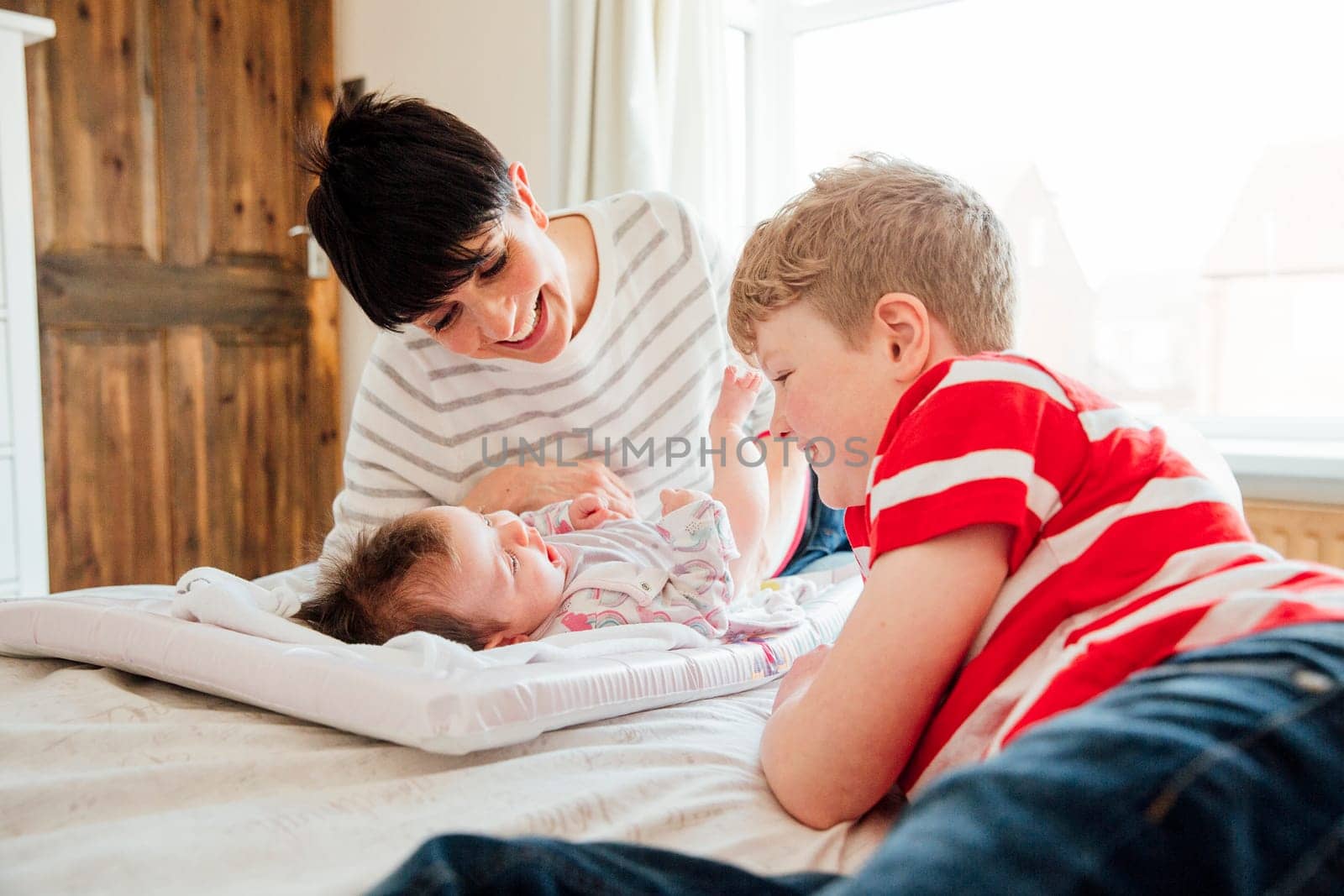 Little boy and his mother are being playful with the baby after changing her nappy on the bed.