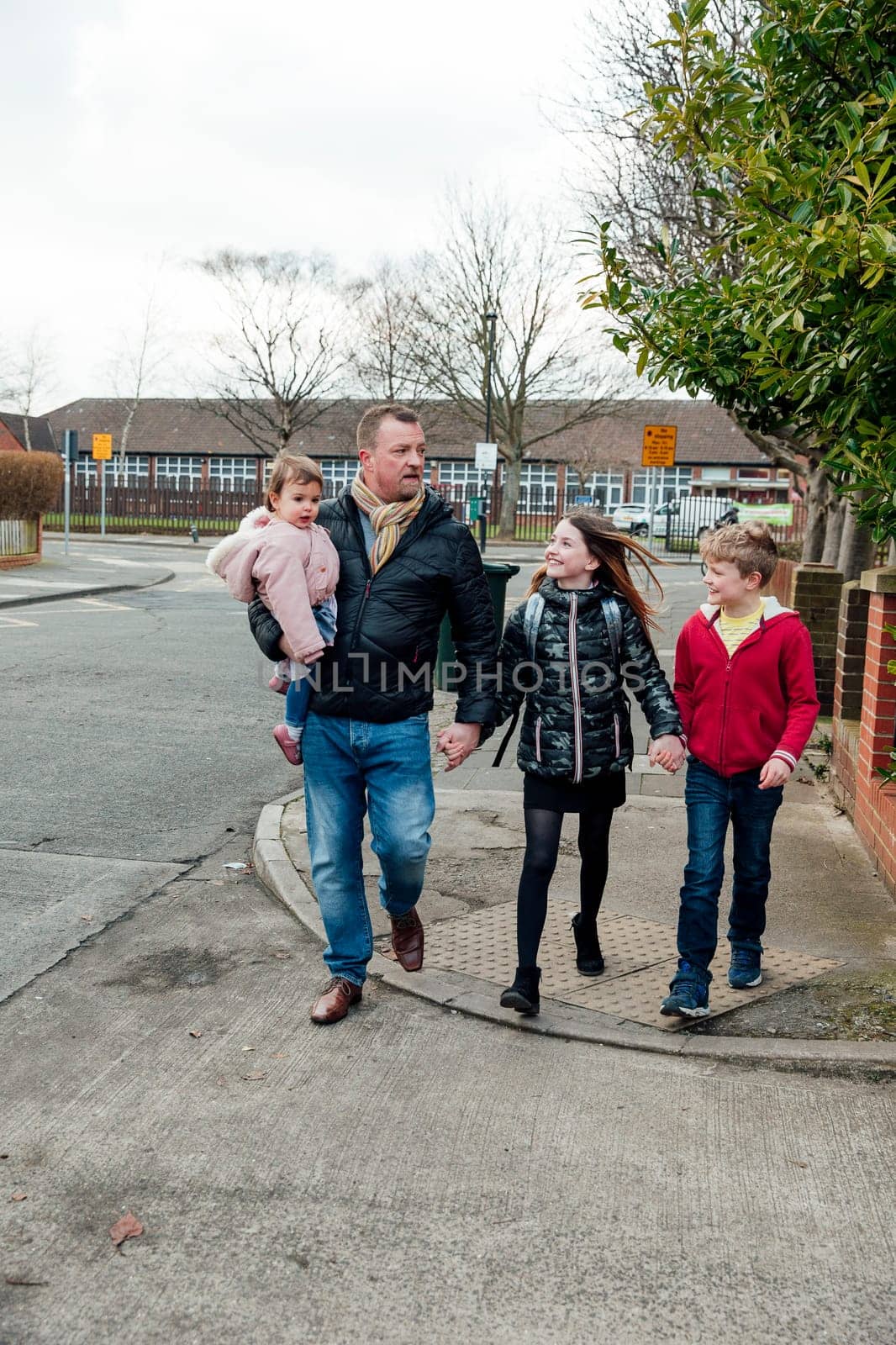 Mature man has just picked up his eldest daughter from school with his other two children. They are talking as they walk home together.