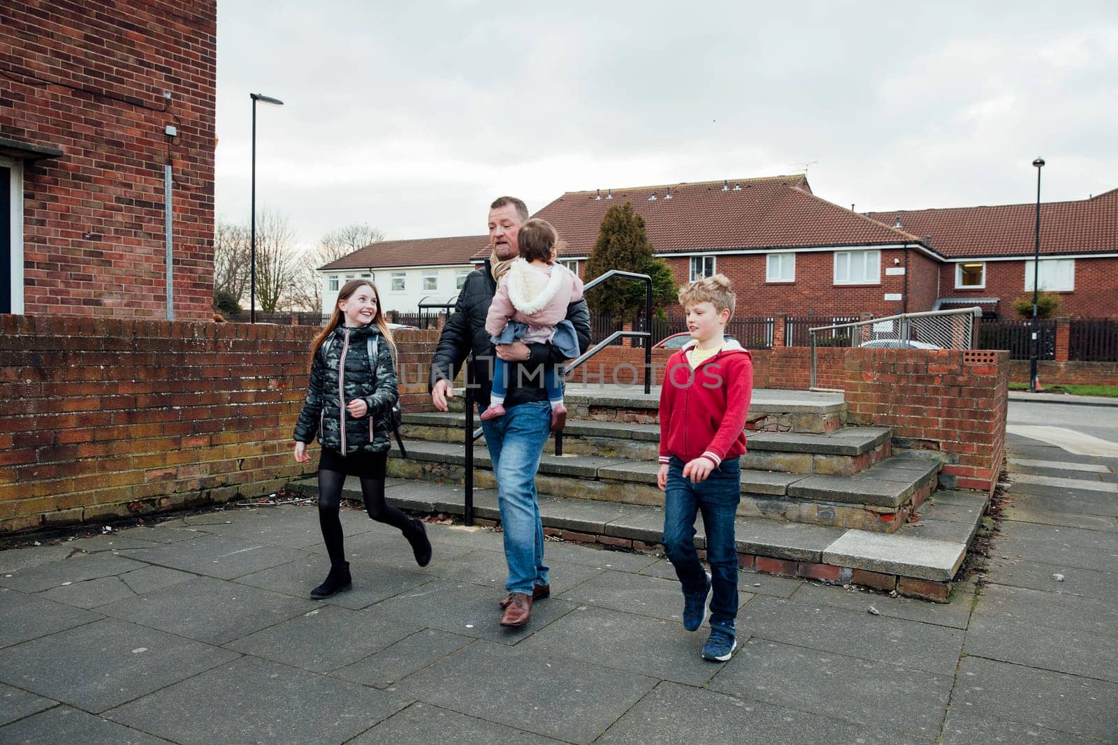 Mature man has just picked up his eldest daughter from school with his other two children. They are talking as they walk home together.