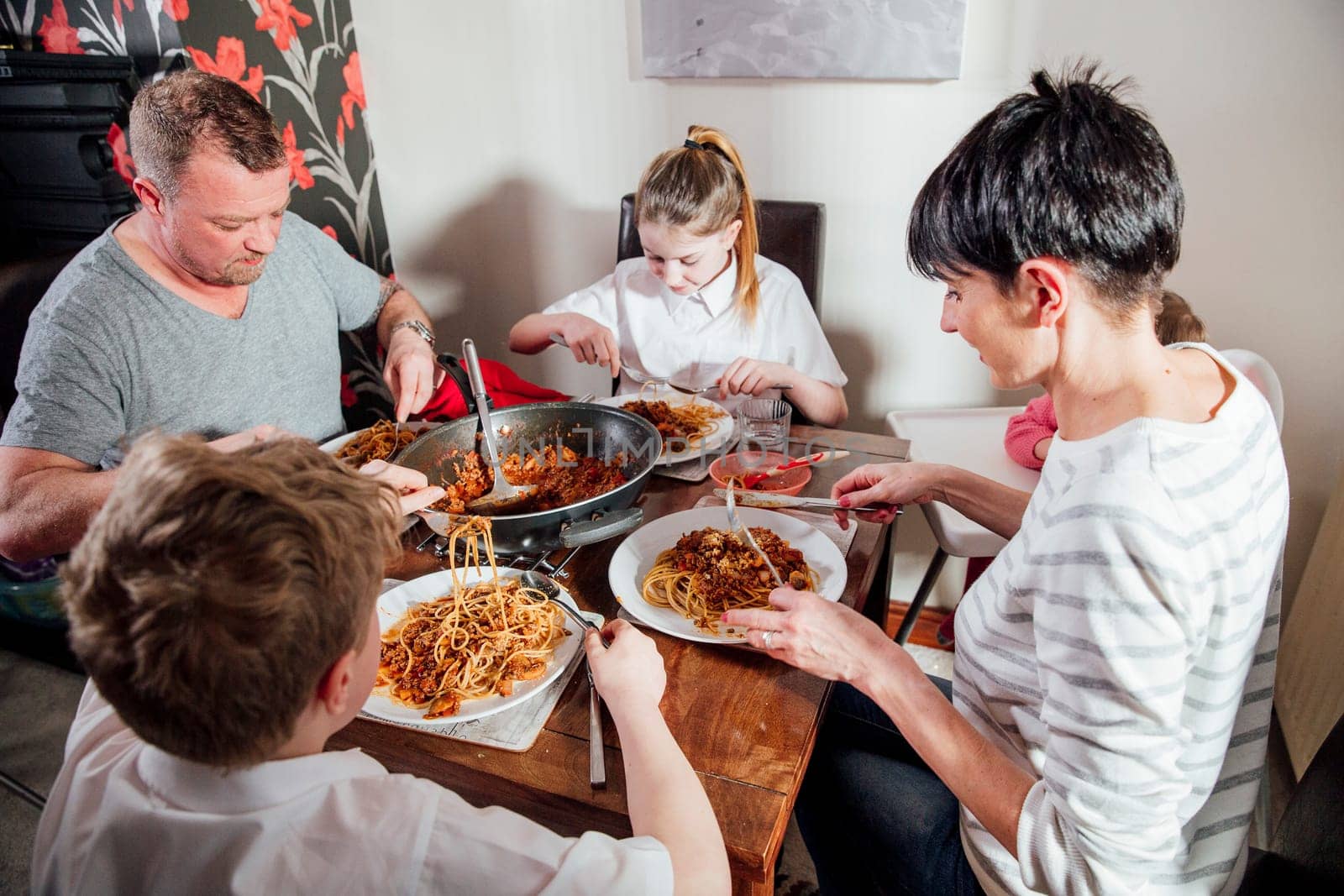 British family enjoying a spagetti bolognese together at home. They are sitting at the dining table with the baby girl in a baby seat.