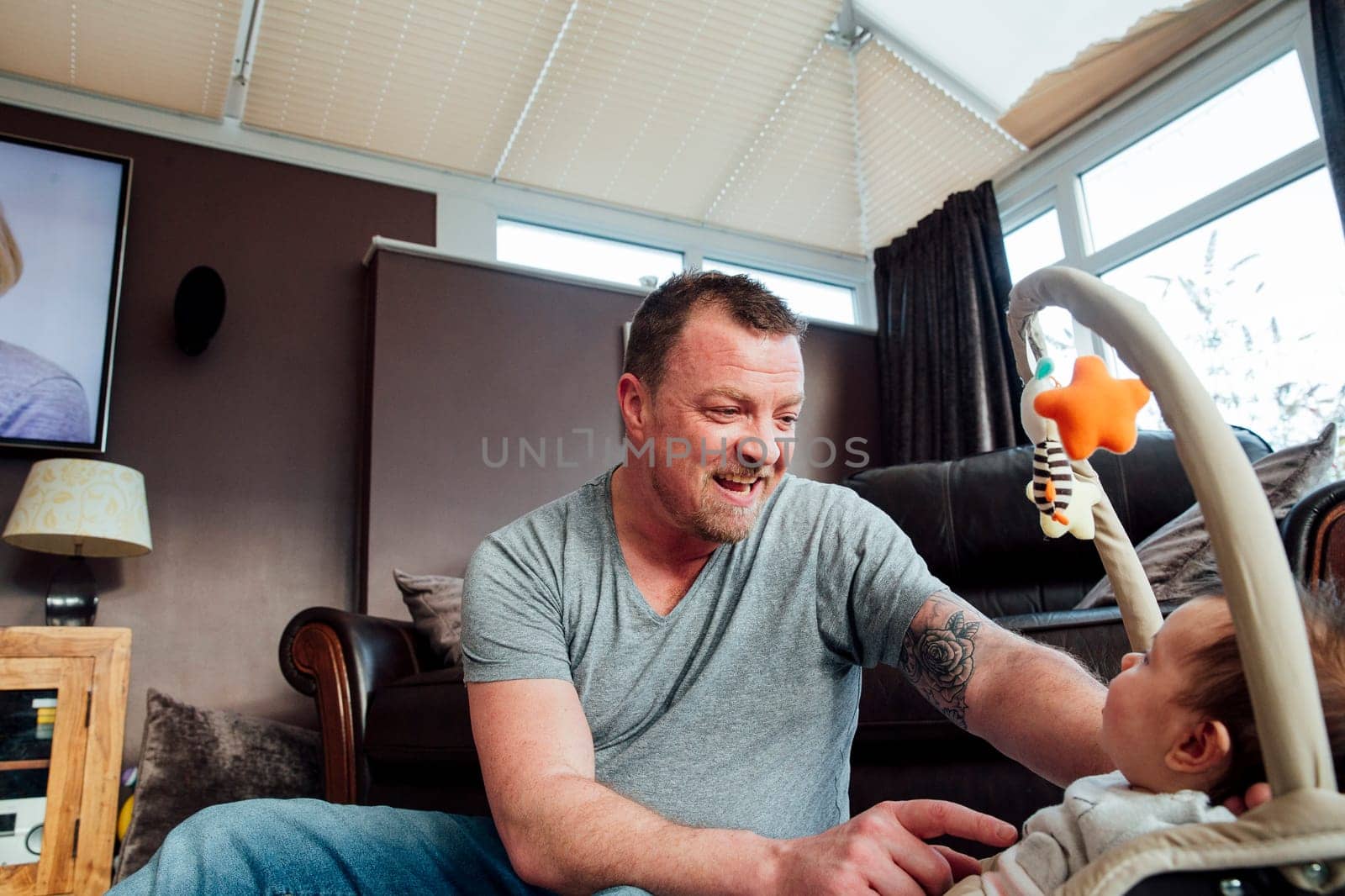 Stay at home father is relaxing in the living room with his baby daughter while she is in her baby bouncer.