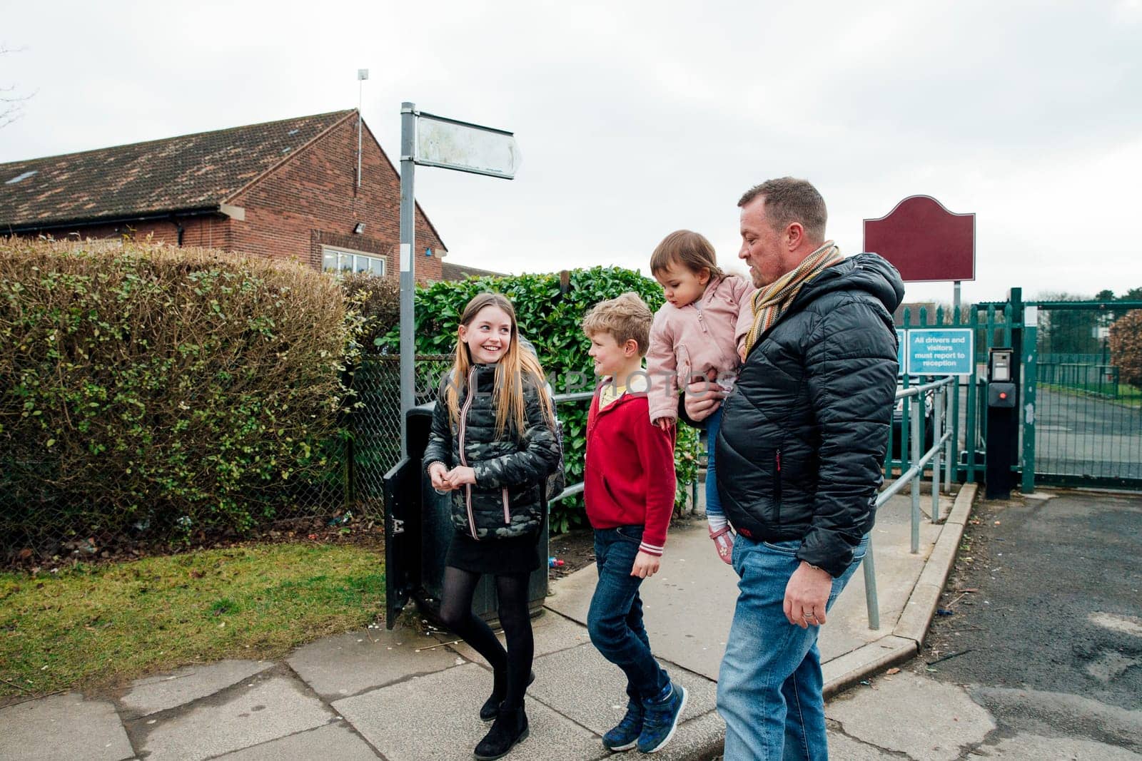Mature man has just picked up his eldest daughter from school with his other two children. They are talking as they walk home together.