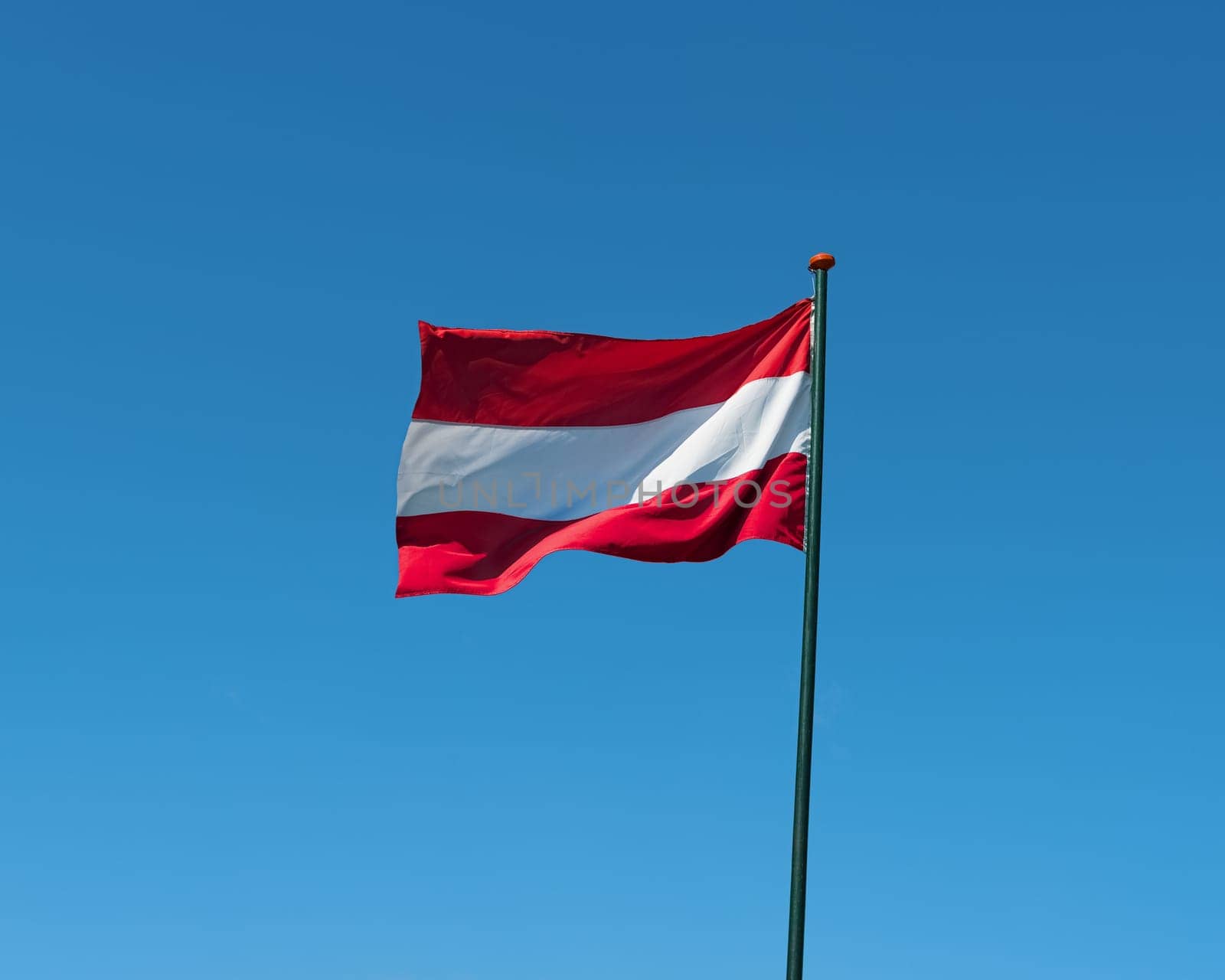 Flag of Austria on flagpole waving in the wind. Austrian national official flag on blue sky background. Patriotic symbol, banner