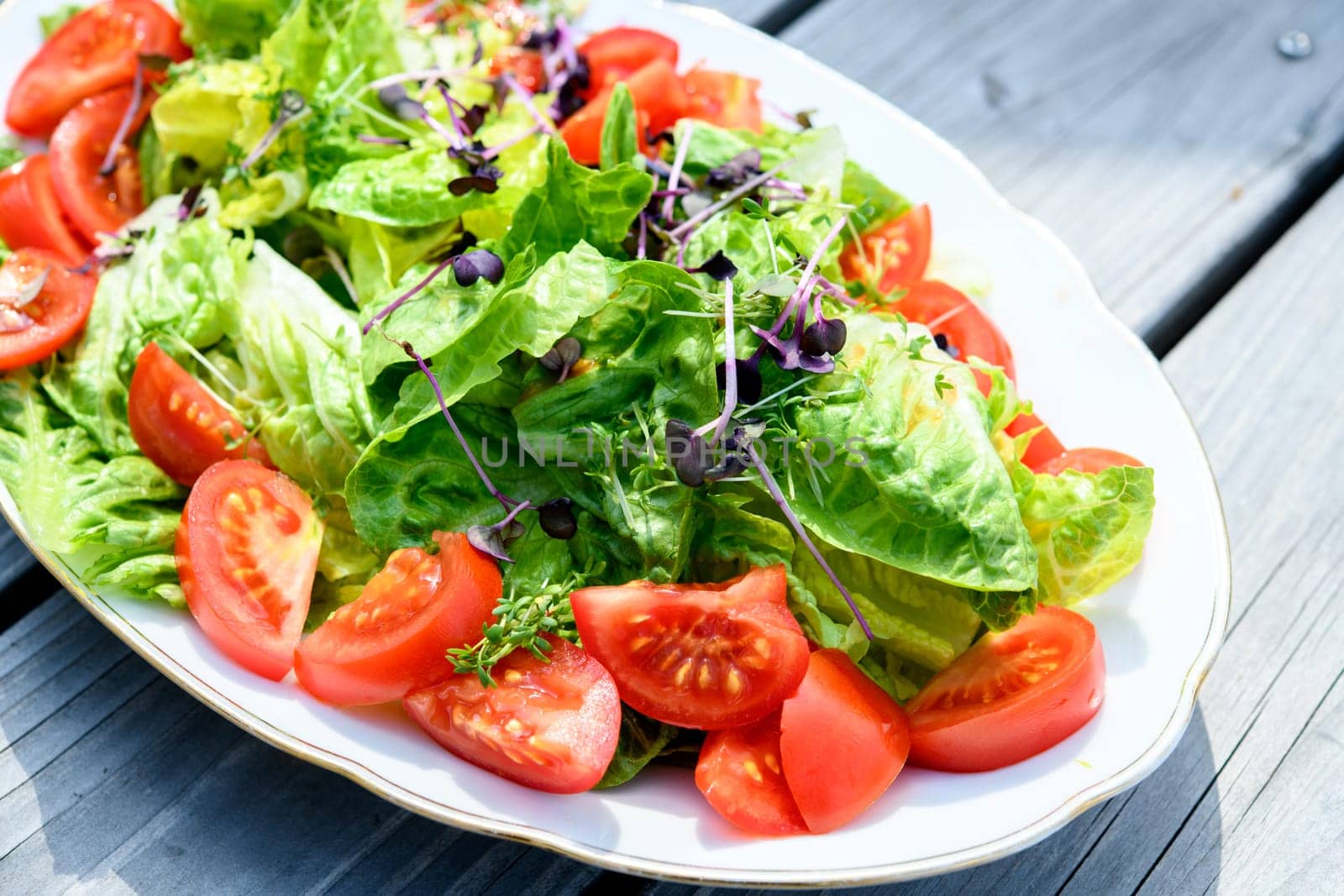 mixed summer salad on plate and wooden ground