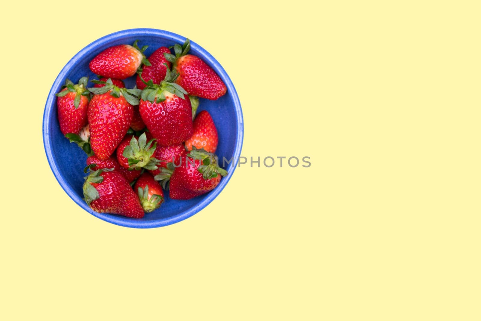 strawberries in blue bowl on pastel yellow ground from above
