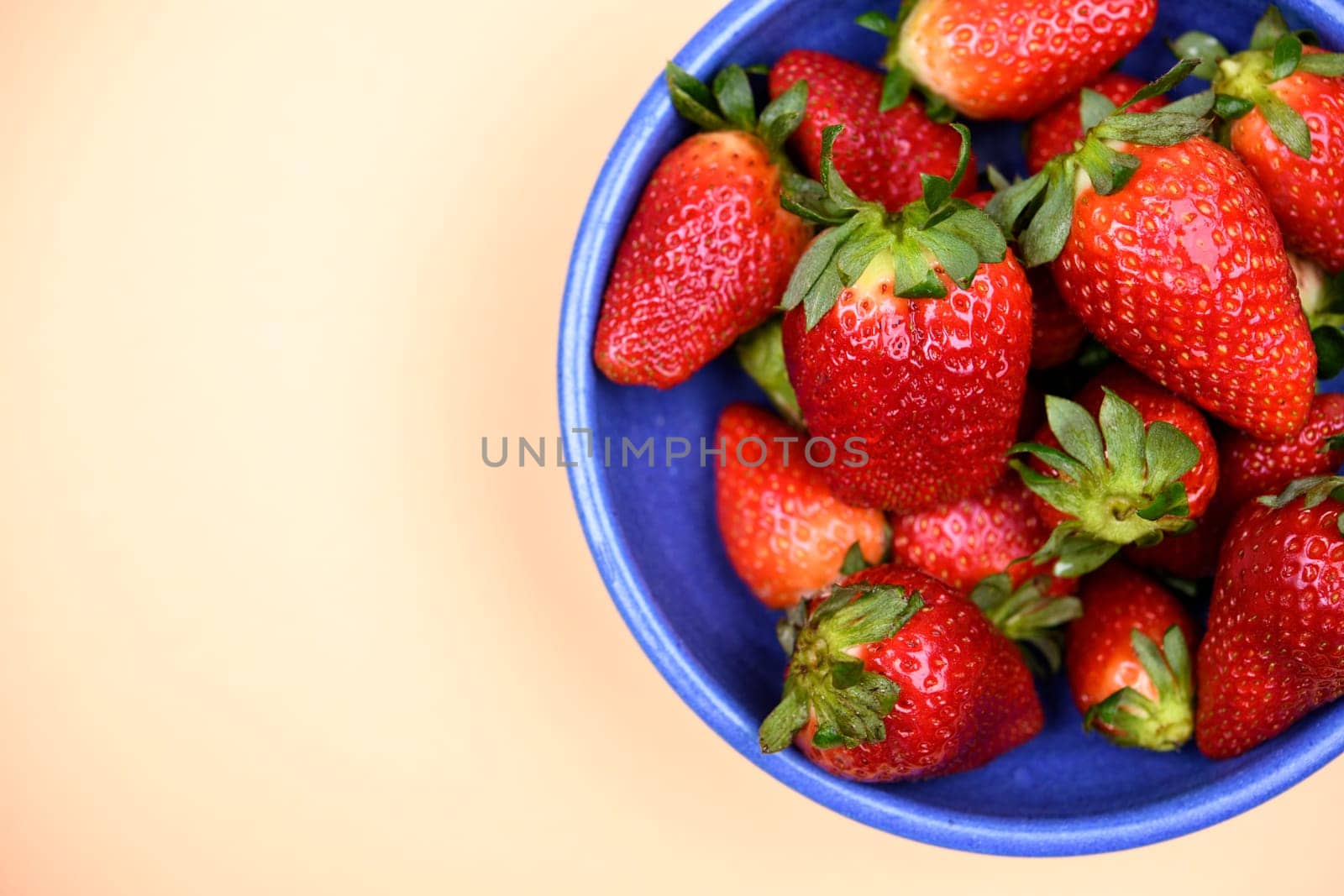 strawberries in blue bowl on pastel orange ground from above