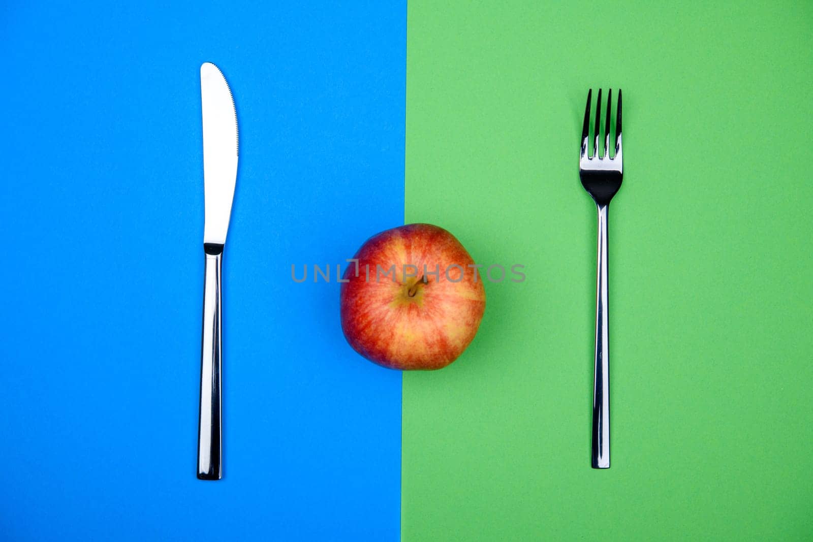red apple from above with knife and fork on blue and green ground