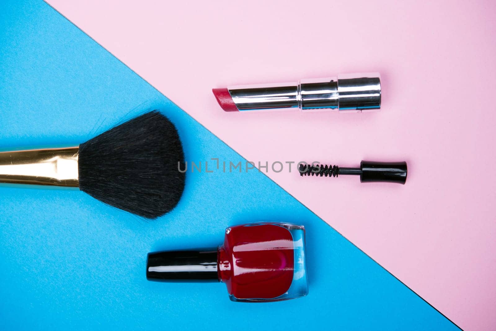 makeup collection with  lipstick, mascara, nail polish and brush from above on blue and pink ground