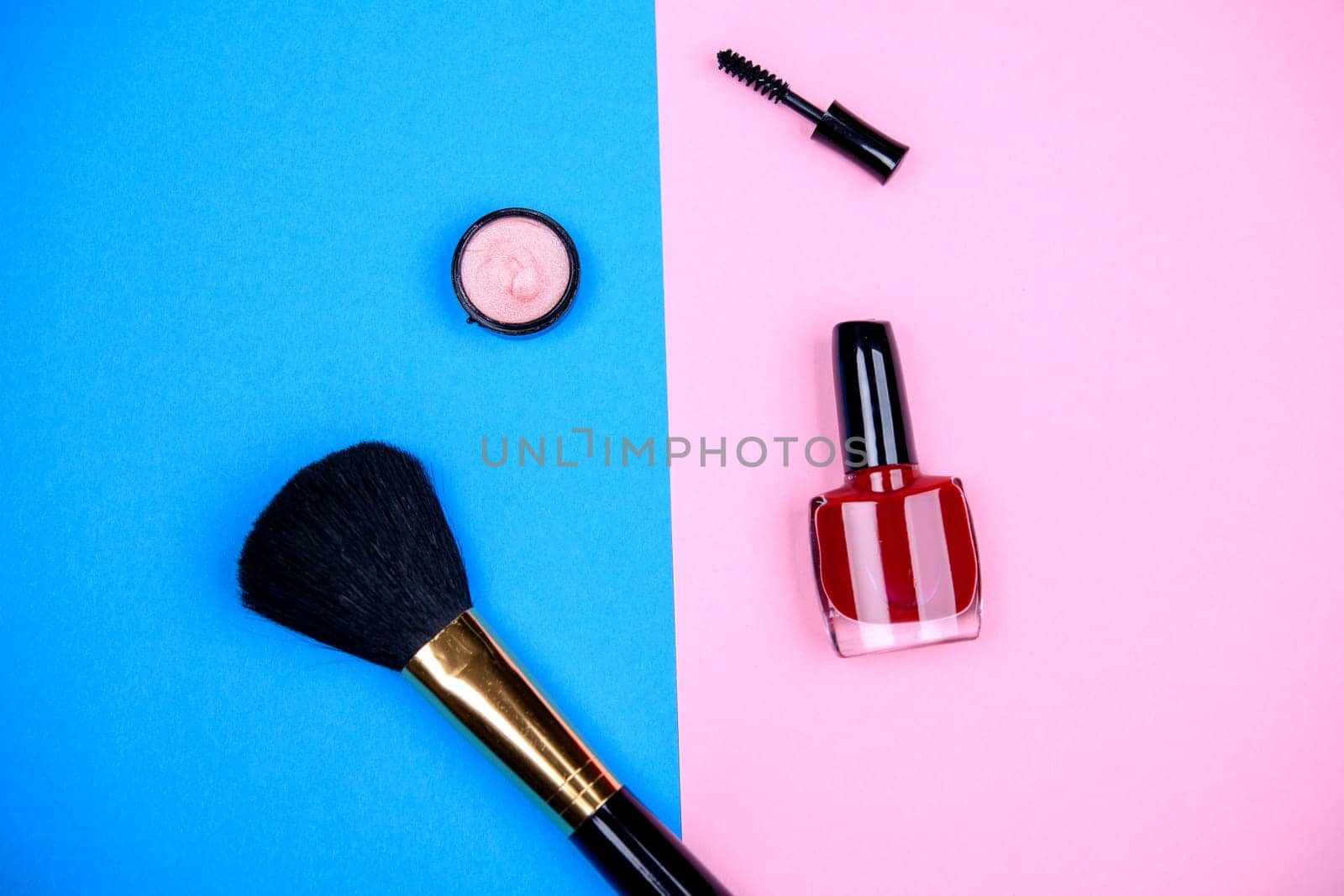 makeup collection with  mascara, nail polish ,eye shadow and brush from above on blue and pink ground
