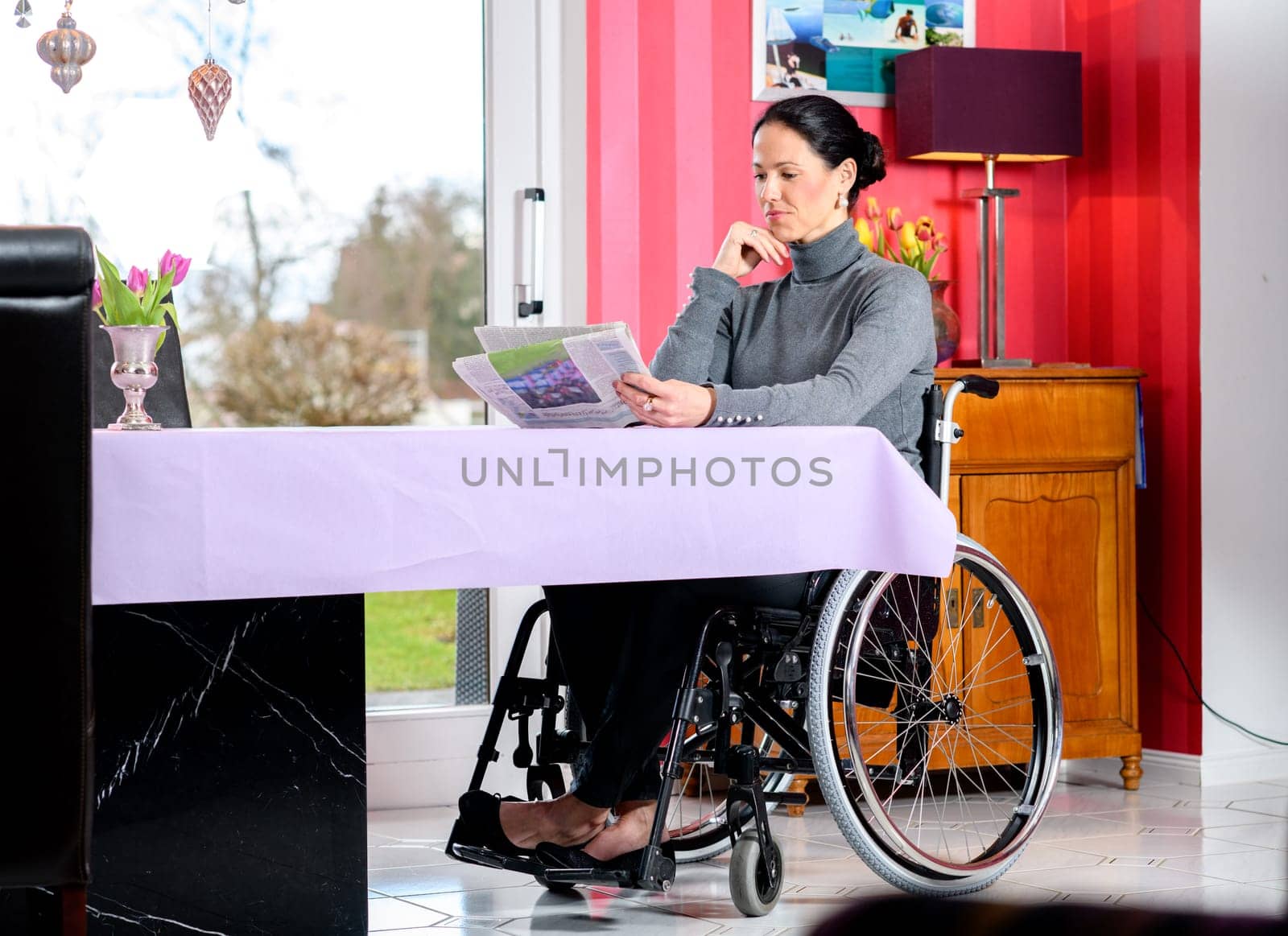 young disabled woman in wheelchair at home reading newspaper and drinking coffee