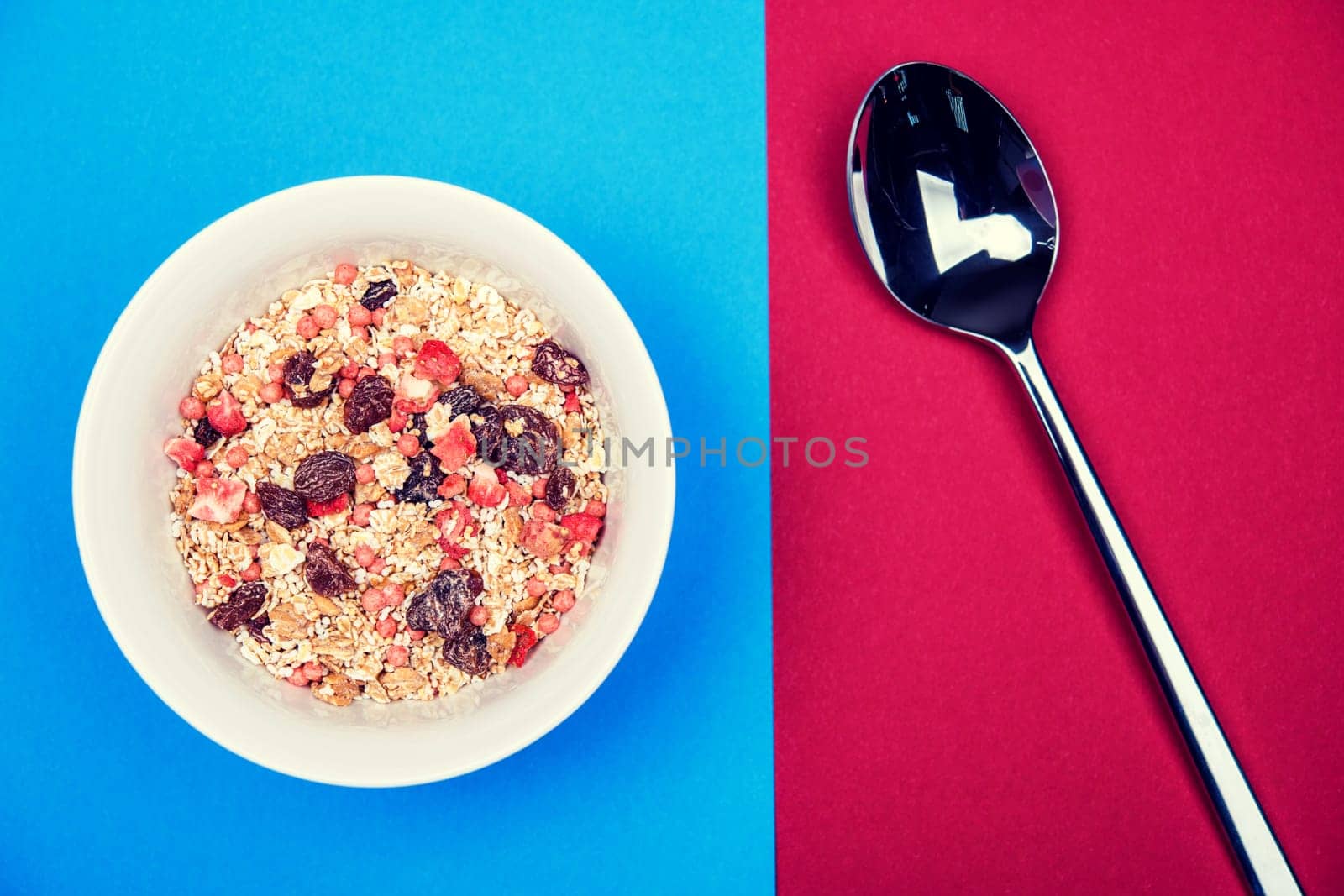 muesli in white bowl on blue and red ground with spoon from above