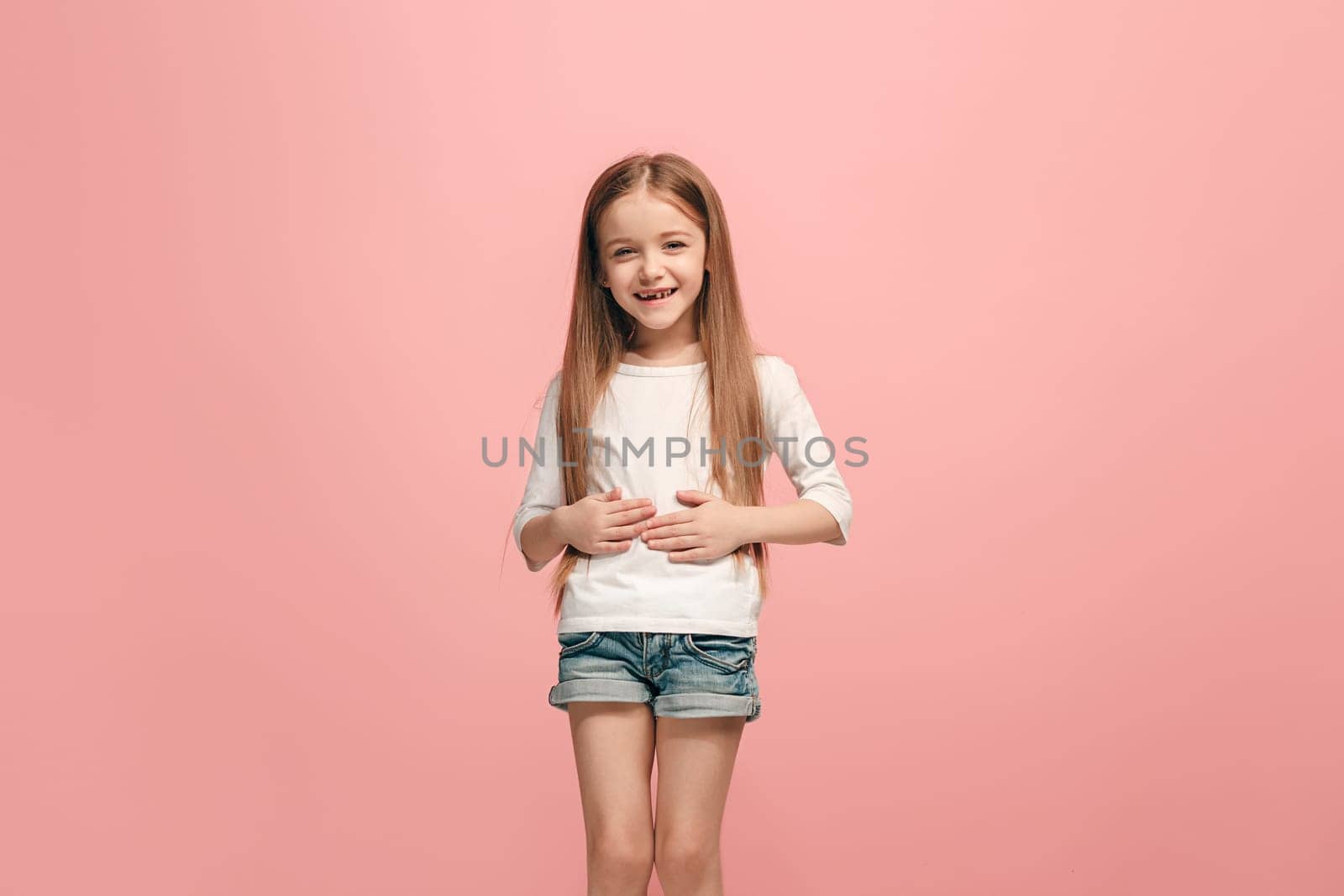 Happy teen girl standing, smiling isolated on trendy pink studio background. Beautiful female half-length portrait. Young satisfy girl. Human emotions, facial expression concept. Front view.