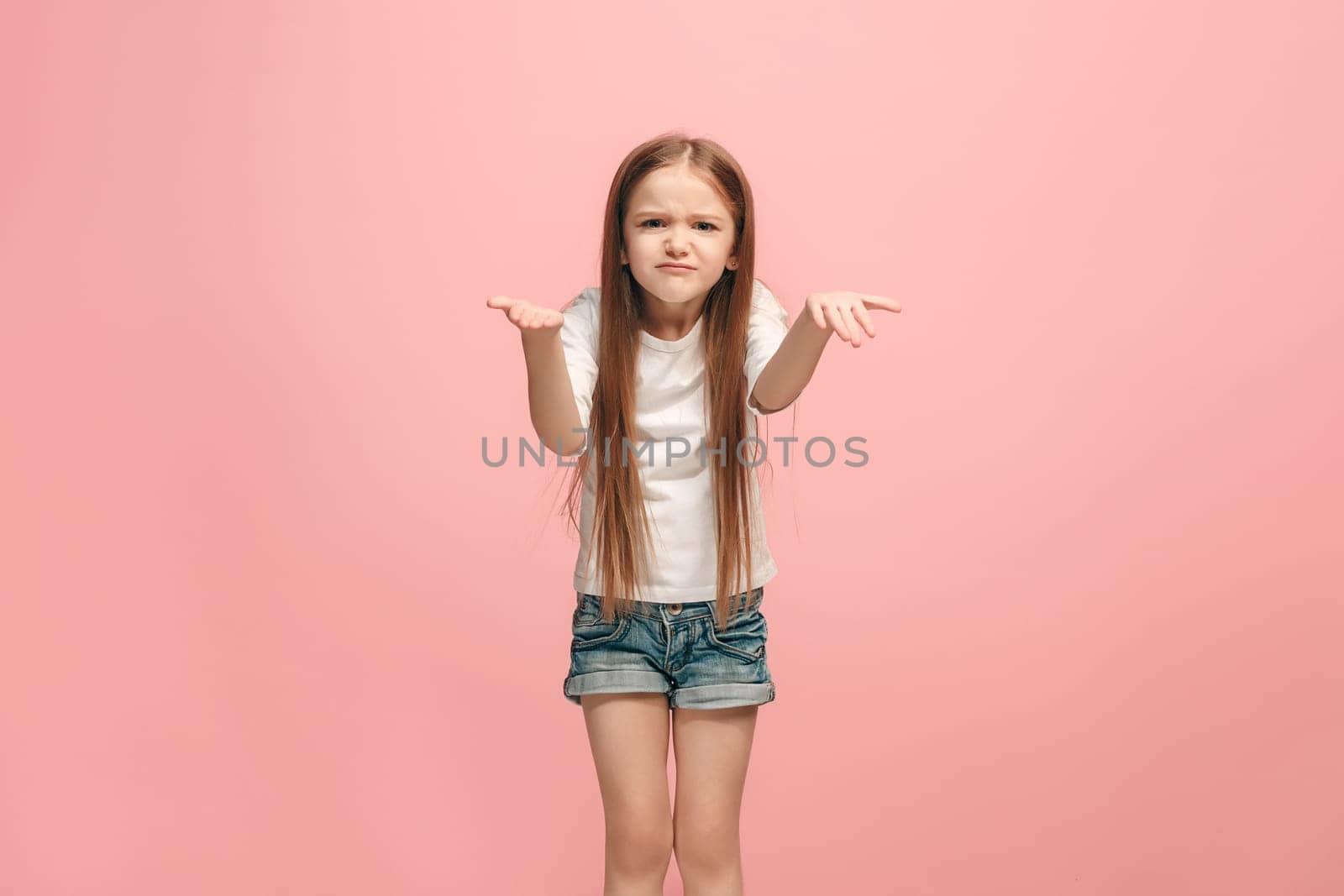 Why is that. Beautiful female half-length portrait on trendy pink studio backgroud. Young emotional surprised, frustrated and bewildered teen girl. Human emotions, facial expression concept.