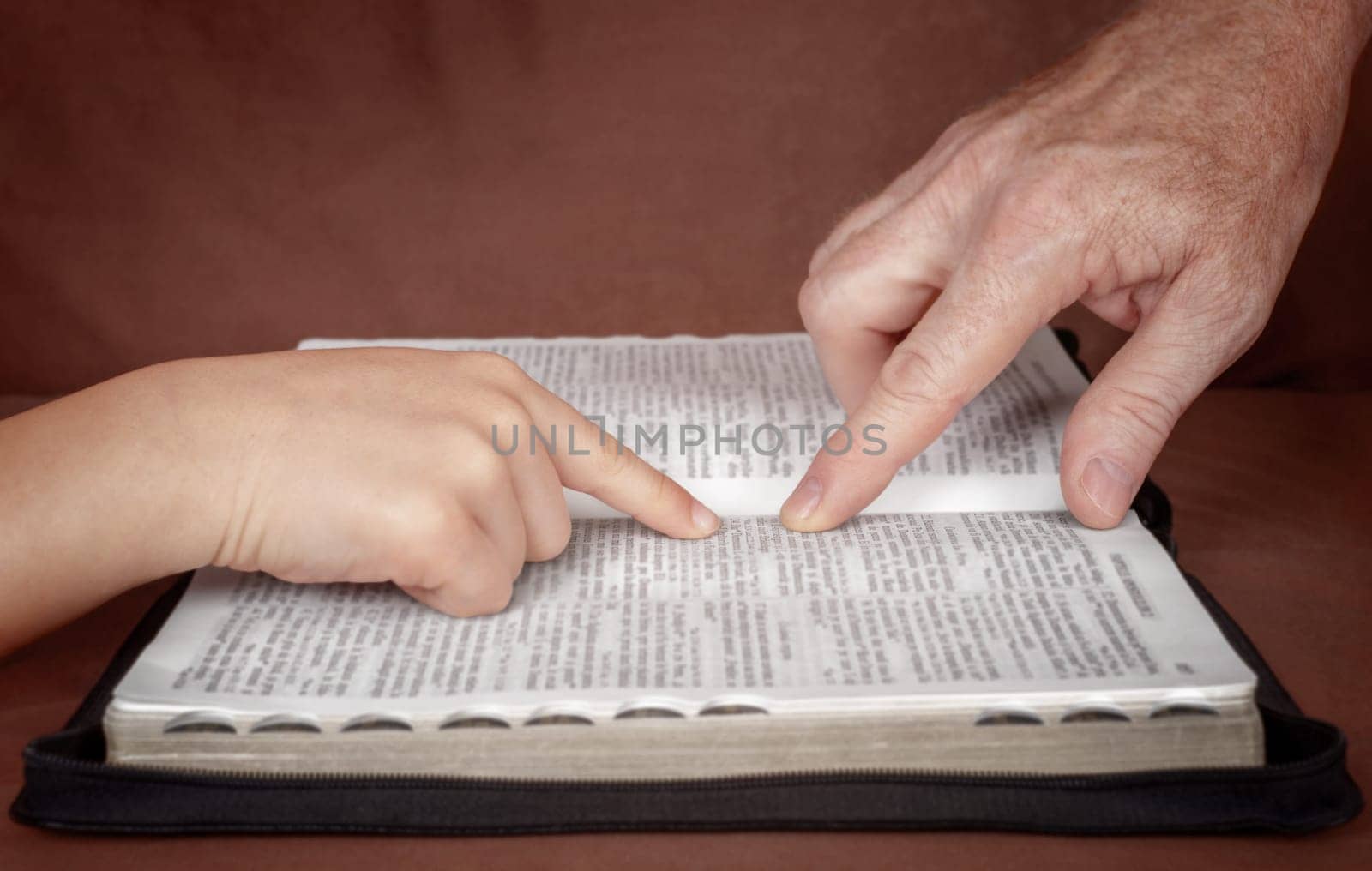 Hand of man pointing something to a child in the Bible book. Teaching a disciple from the Bible.