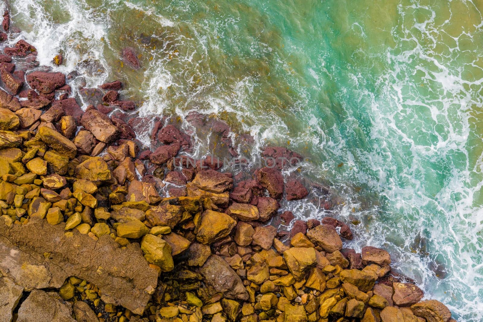 Top aerial view of blue waves crashing on rocky Australian coastline. Summer seascape with birds eye view shot over ocean waves and cliffs. Travel concept background