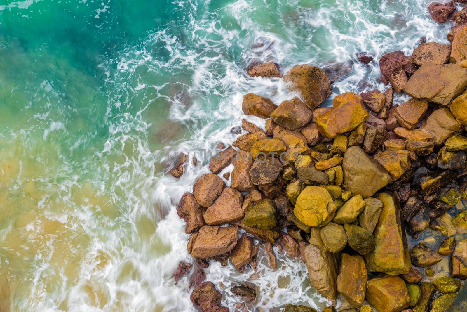 Top aerial view of blue waves crashing on rocky Australian coastline. Summer seascape with birds eye view shot over ocean waves and cliffs. Travel concept background