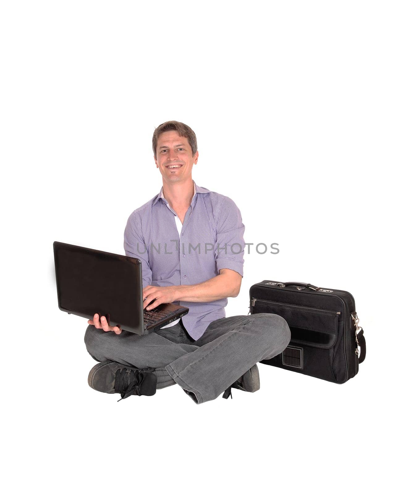 A young smiling man sitting on the floor with his laptop and briefcase.looking up and smiling, isolated for white background.