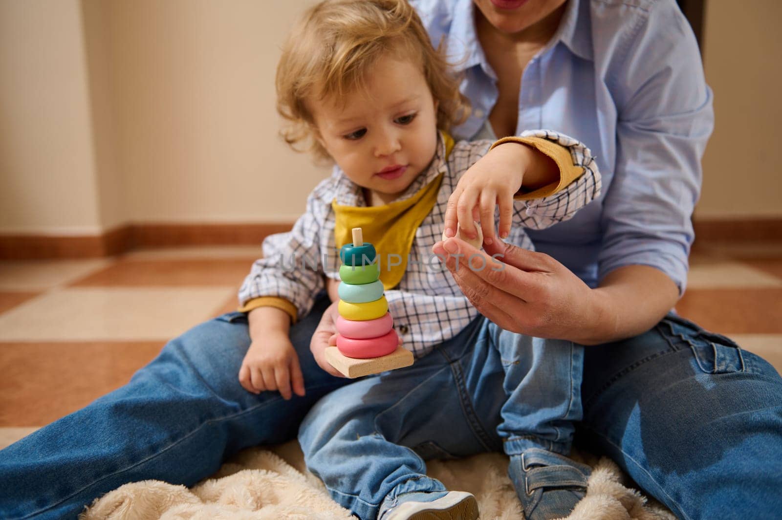 A mother sits with her toddler son, helping him play with colorful stacking toys. A sweet and enriching moment that fosters cognitive development and emotional bonding.