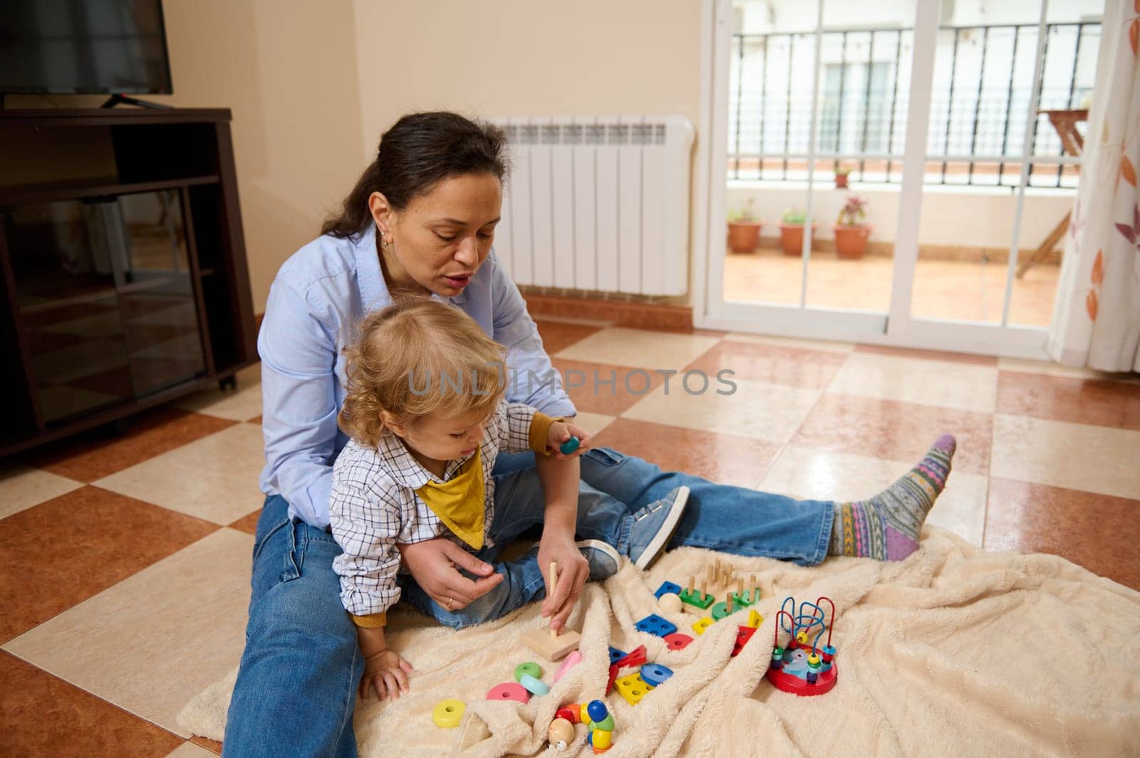 A loving mother and her child bond over playing with colorful educational toys on a cozy blanket indoors, showcasing warmth and joy.
