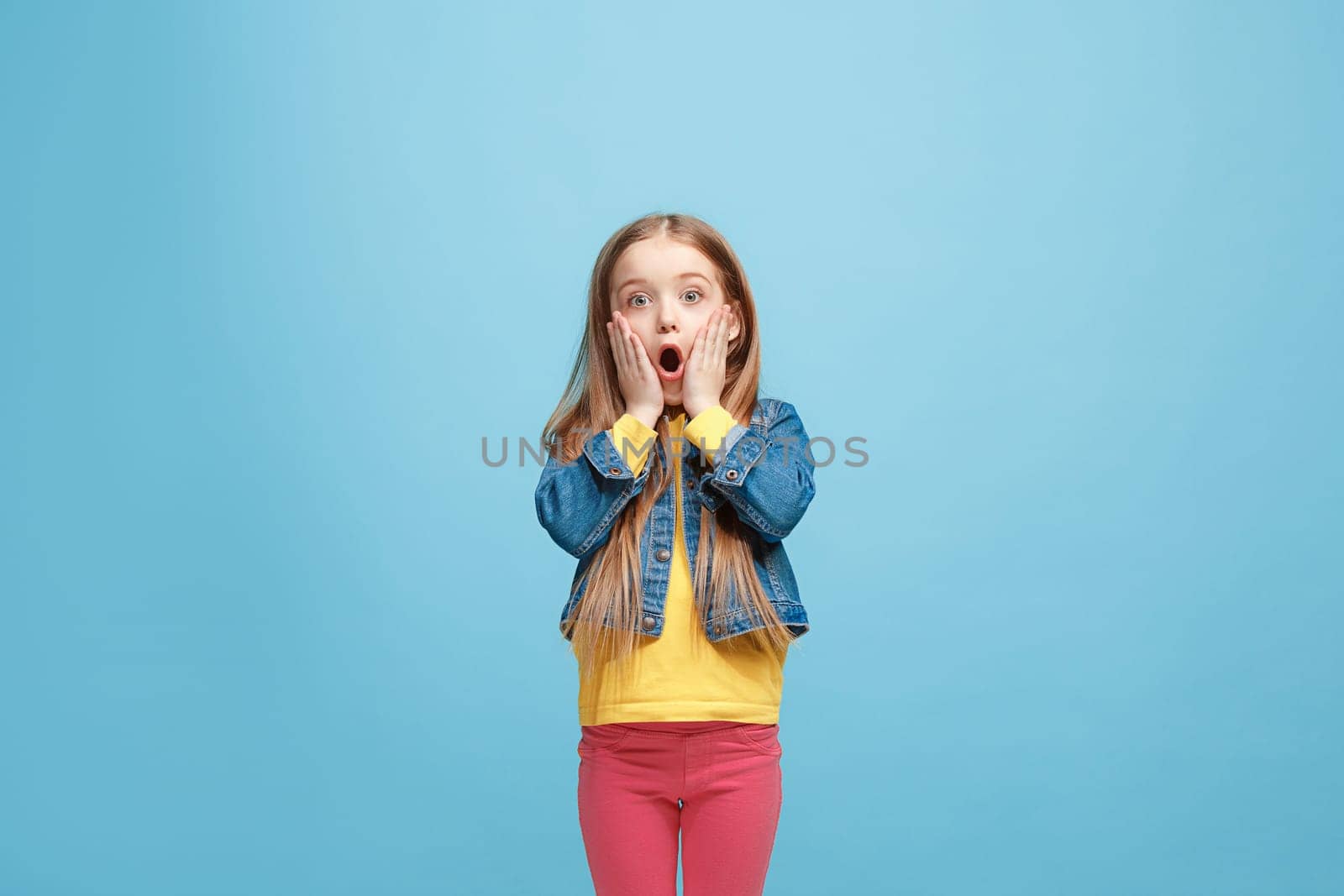 Wow. Beautiful female half-length front portrait isolated on blue studio backgroud. Young emotional surprised teen girl standing with open mouth. Human emotions, facial expression concept. Trendy colors