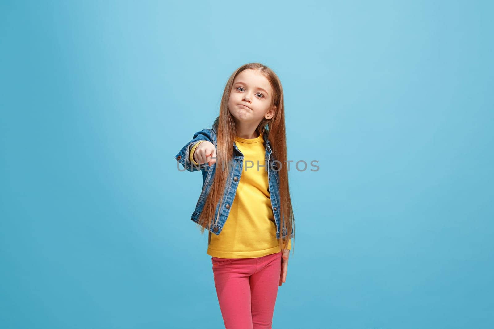 I choose you and order. The smiling teen girl pointing to camera, half length closeup portrait on blue studio background. The human emotions, facial expression concept. Front view. Trendy colors