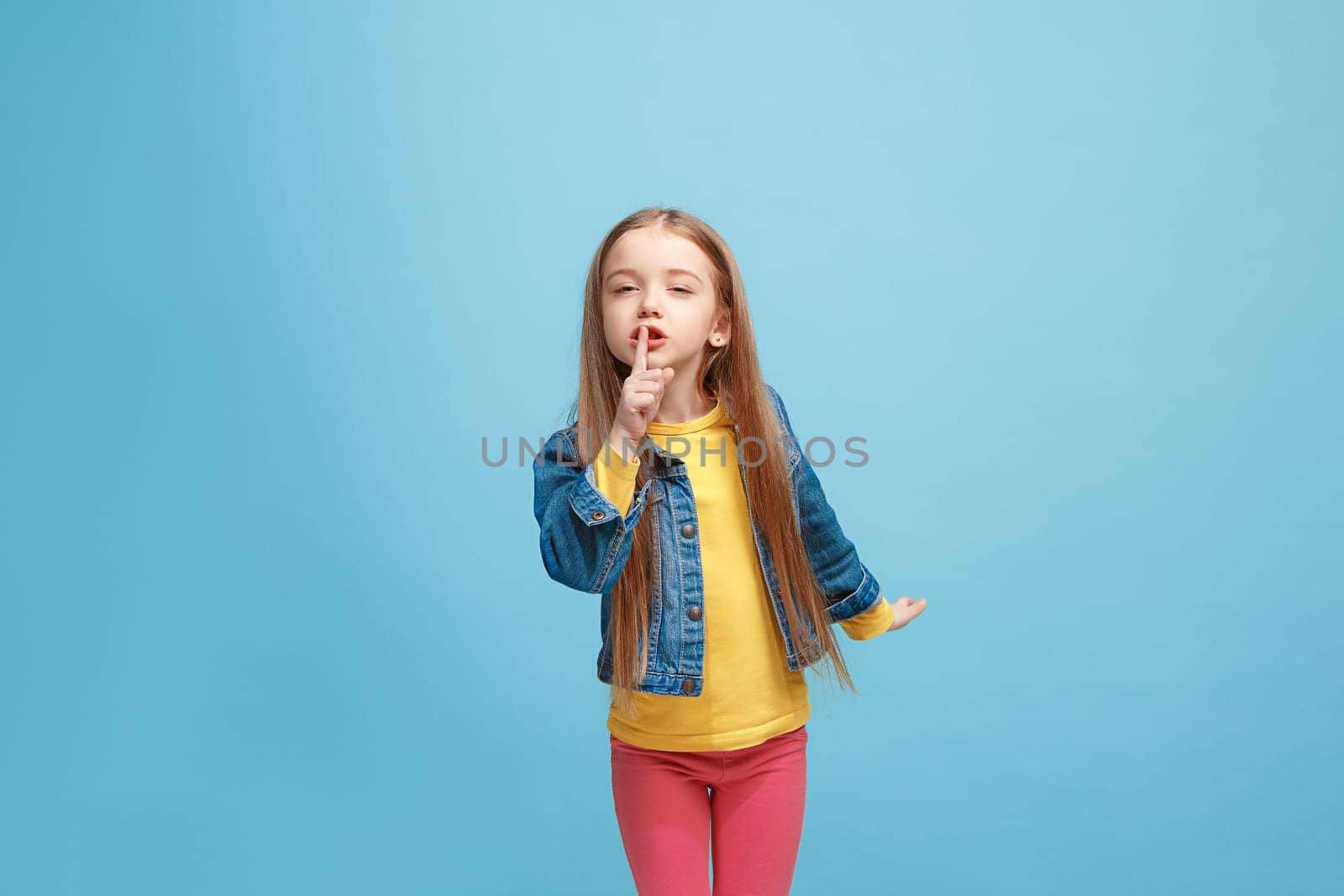 Secret, gossip concept. Young teen girl whispering a secret behind her hand isolated on trendy blue studio background. Young emotional girl. Human emotions, facial expression concept.