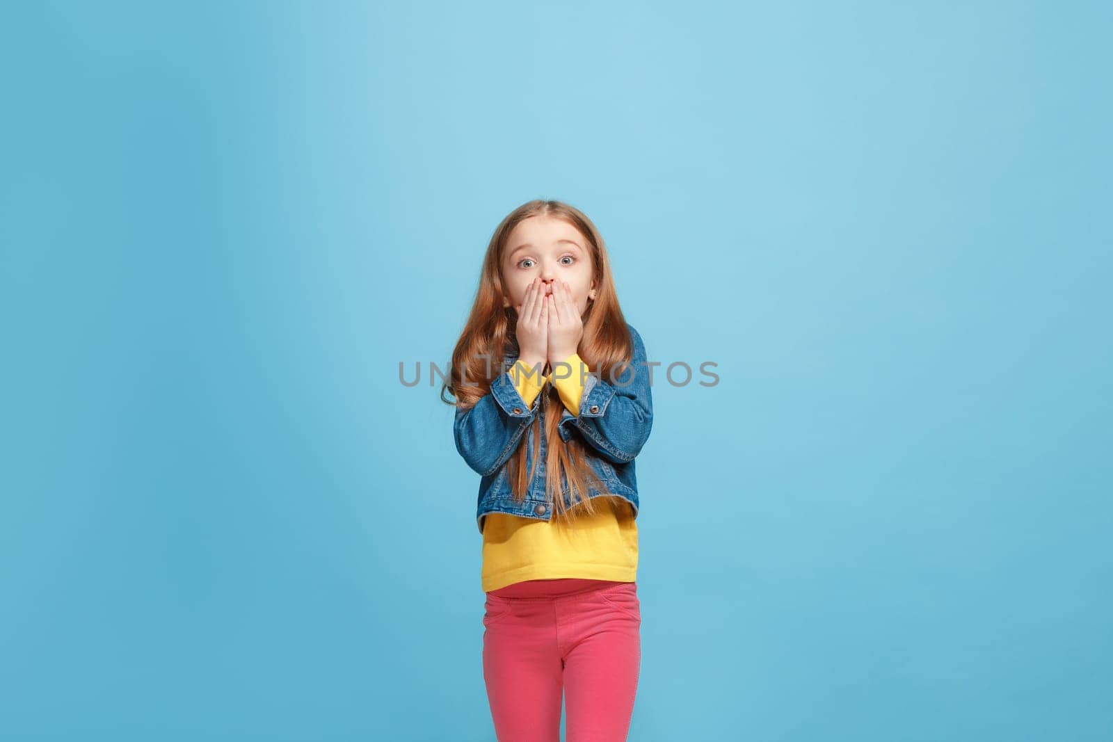 Wow. Beautiful female half-length front portrait isolated on blue studio backgroud. Young emotional surprised teen girl standing with open mouth. Human emotions, facial expression concept. Trendy colors