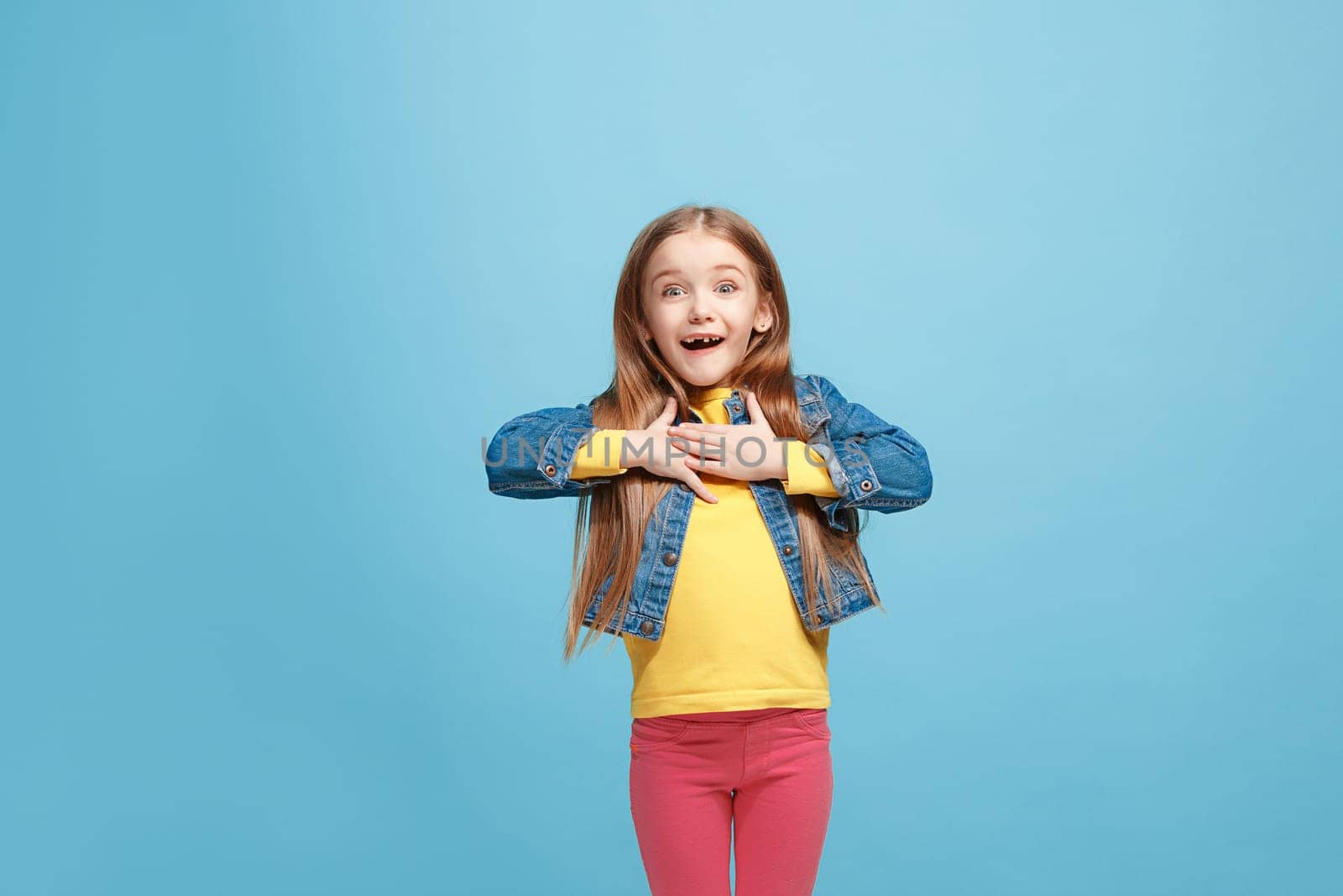 Wow. Beautiful female half-length front portrait isolated on blue studio backgroud. Young emotional surprised teen girl standing with open mouth. Human emotions, facial expression concept. Trendy colors