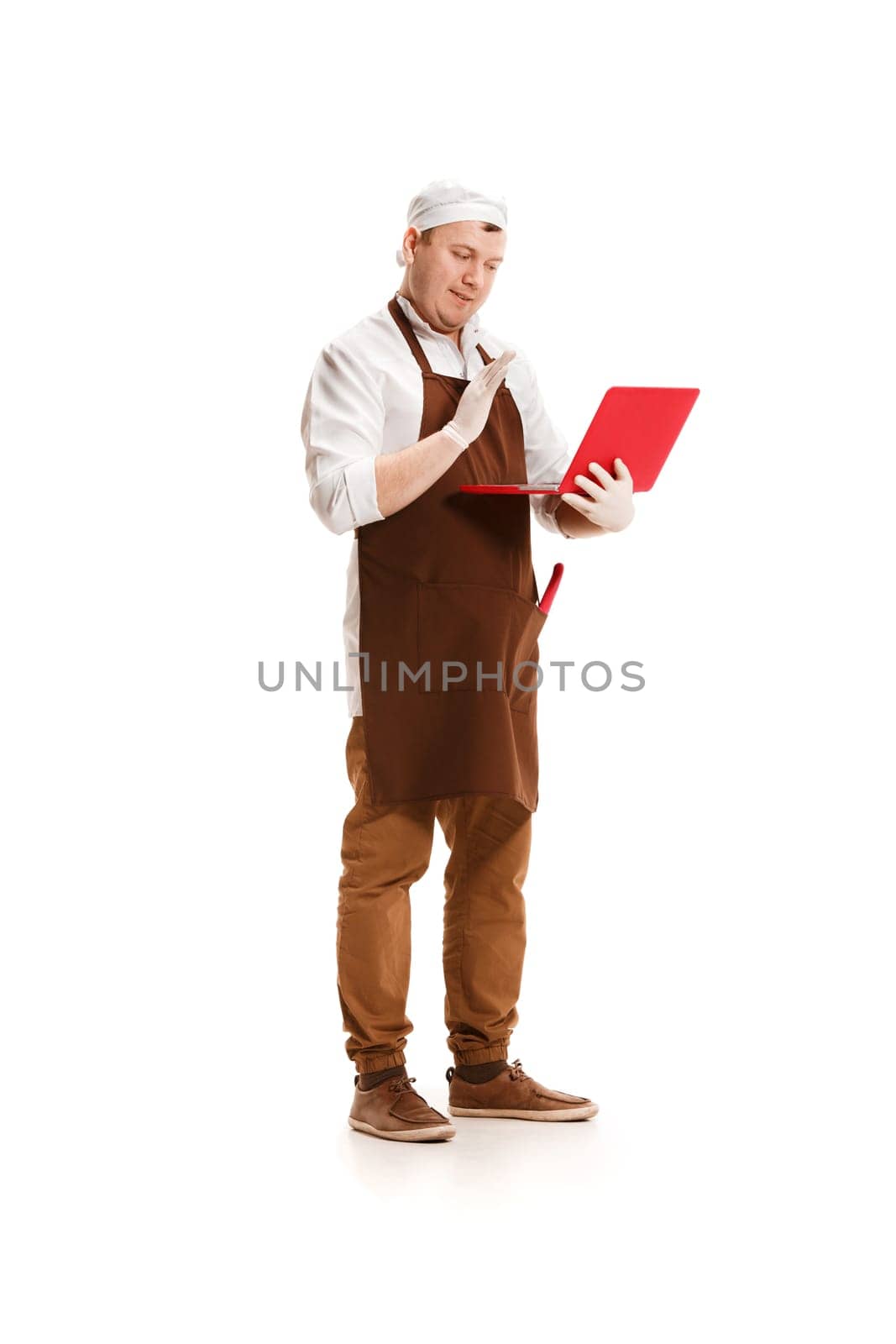 Serious butcher posing with a laptop isolated on white studio background. The young caucasian male model in full-length. Butcher, professional concept
