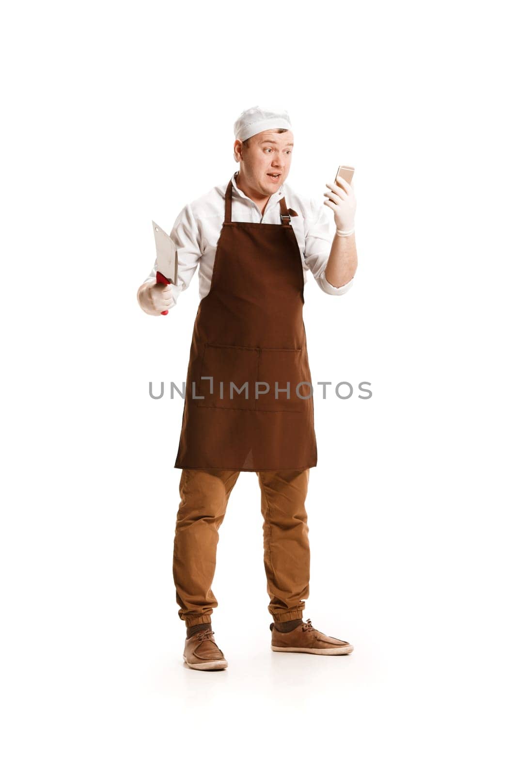 Smiling butcher posing with a knife and mobile phone isolated on white studio background. The young caucasian male model in full-length. Butcher, knife, professional concept