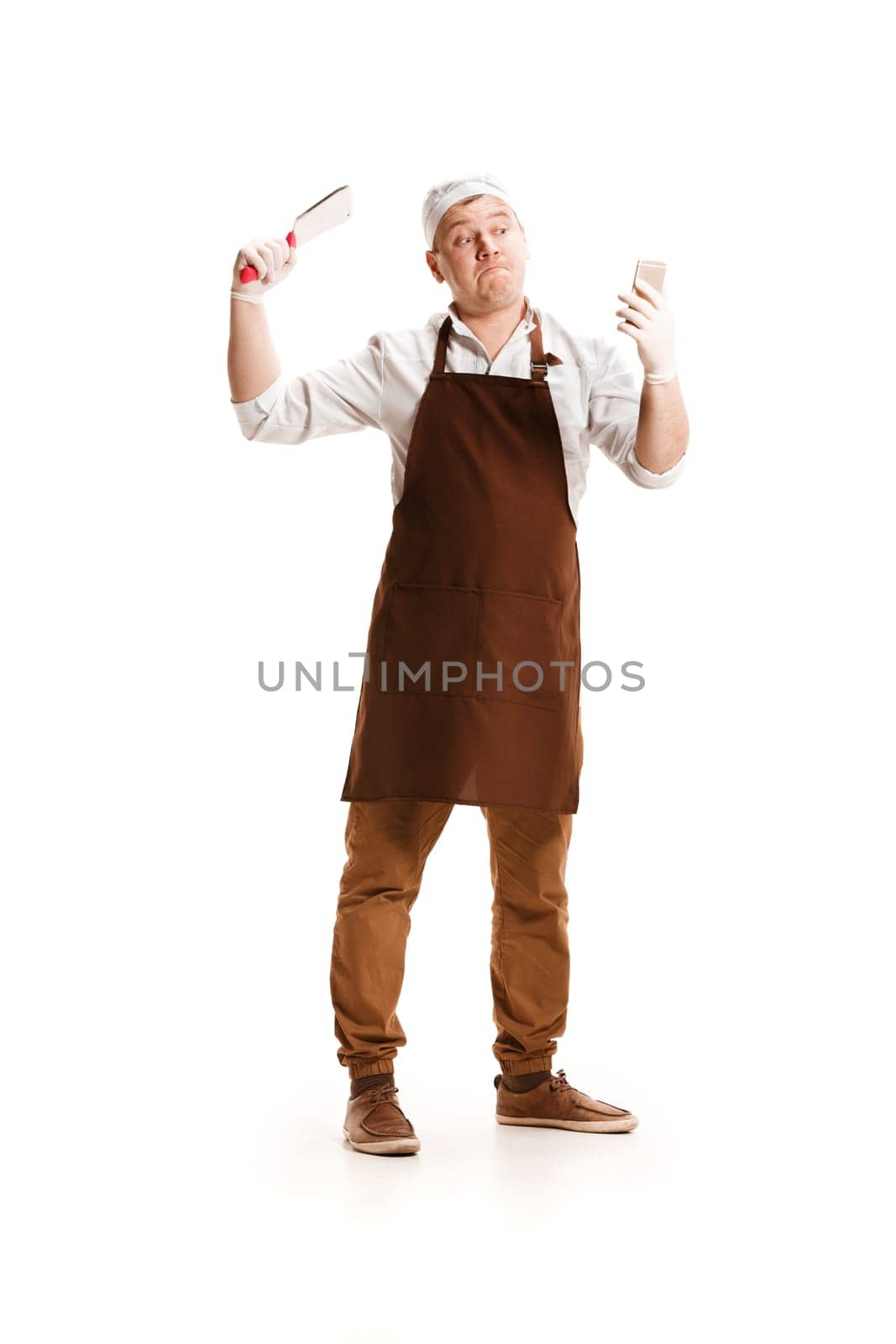 Smiling butcher posing with a knife and mobile phone isolated on white studio background. The young caucasian male model in full-length. Butcher, knife, professional concept