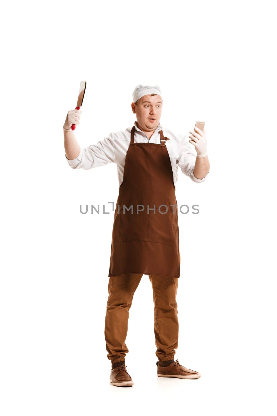 Smiling butcher posing with a knife and mobile phone isolated on white studio background. The young caucasian male model in full-length. Butcher, knife, professional concept