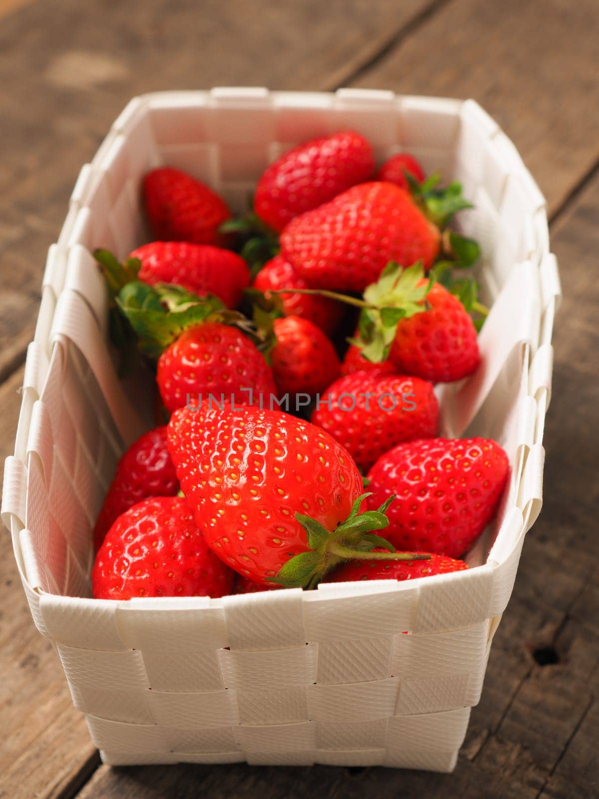 Fresh organic strawberries in a white basket on a rustic wooden table