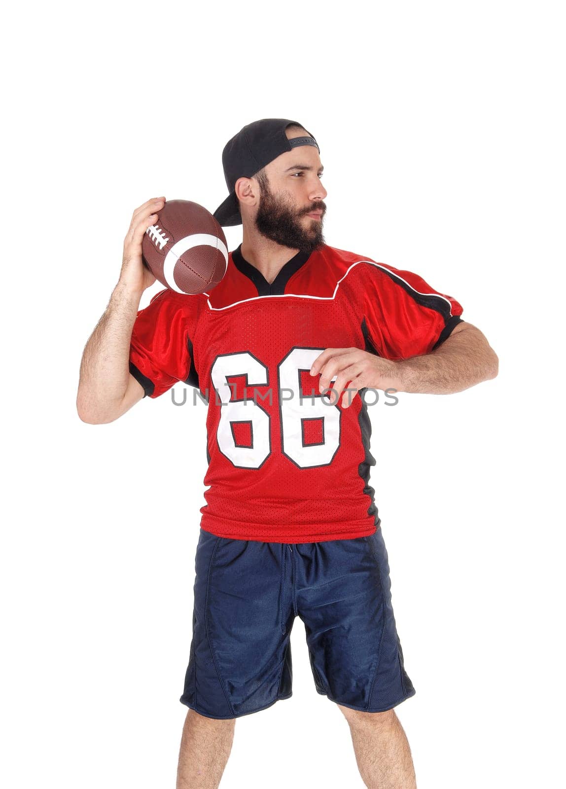 A young football player standing in his uniform and a beard ready to.throw his football, isolated for white background.