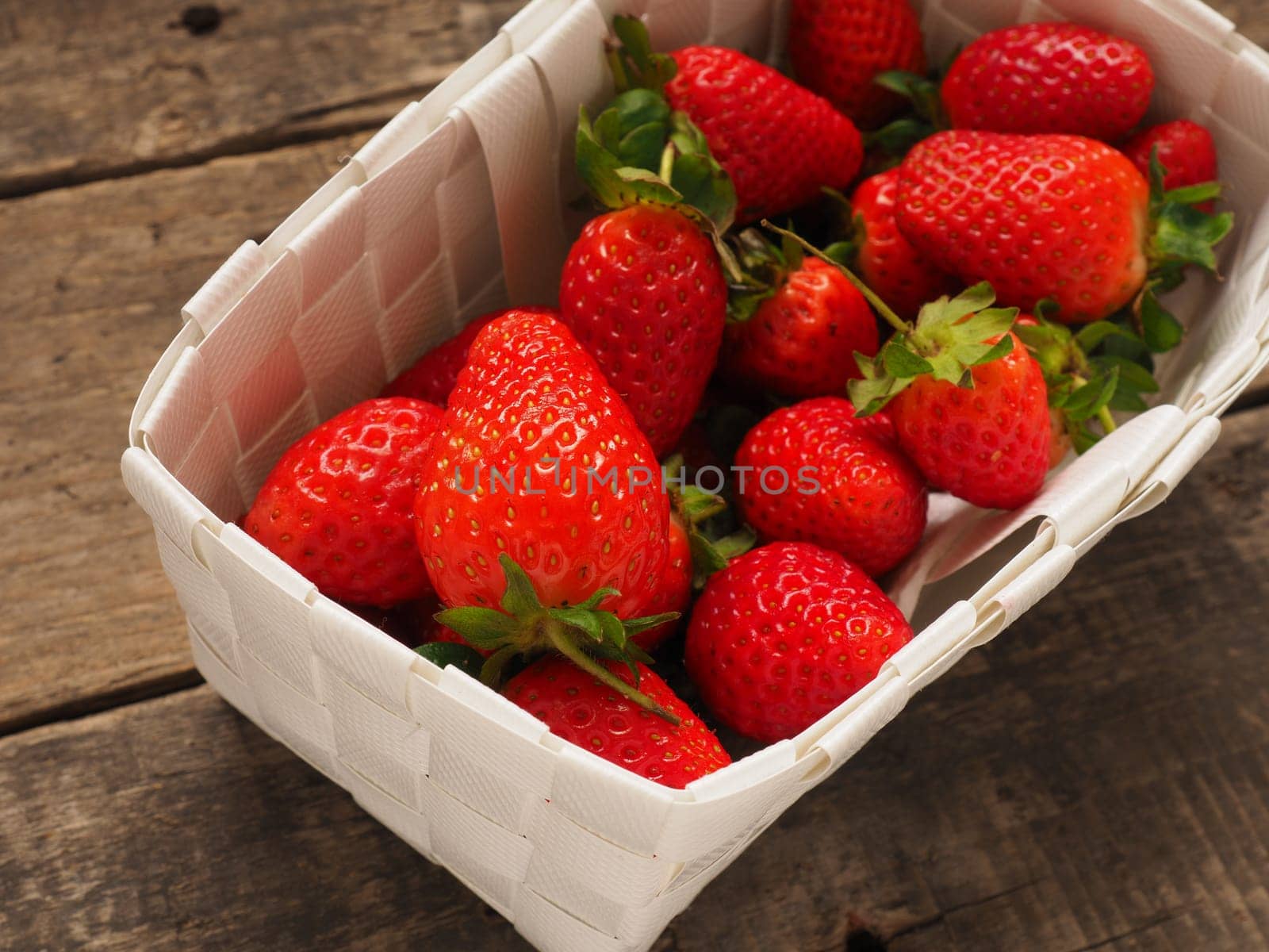Fresh organic strawberries in a white basket on a rustic wooden table
